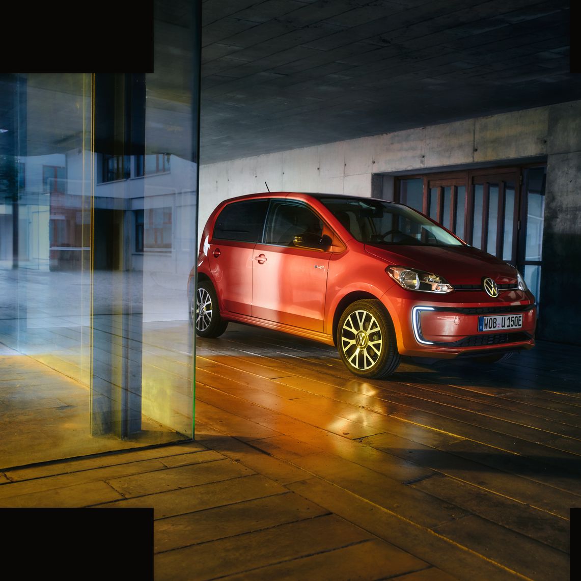 Червен Volkswagen e-up! паркиран в модерна градска сграда с ефектно осветление