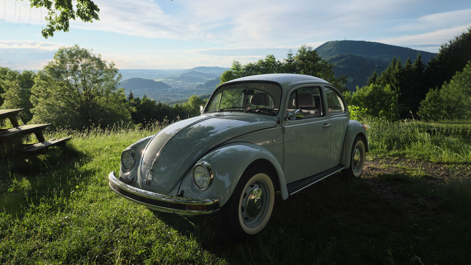 Ретро Volkswagen Beetle в светлосин цвят паркиран на поляна с изглед към планини и гори