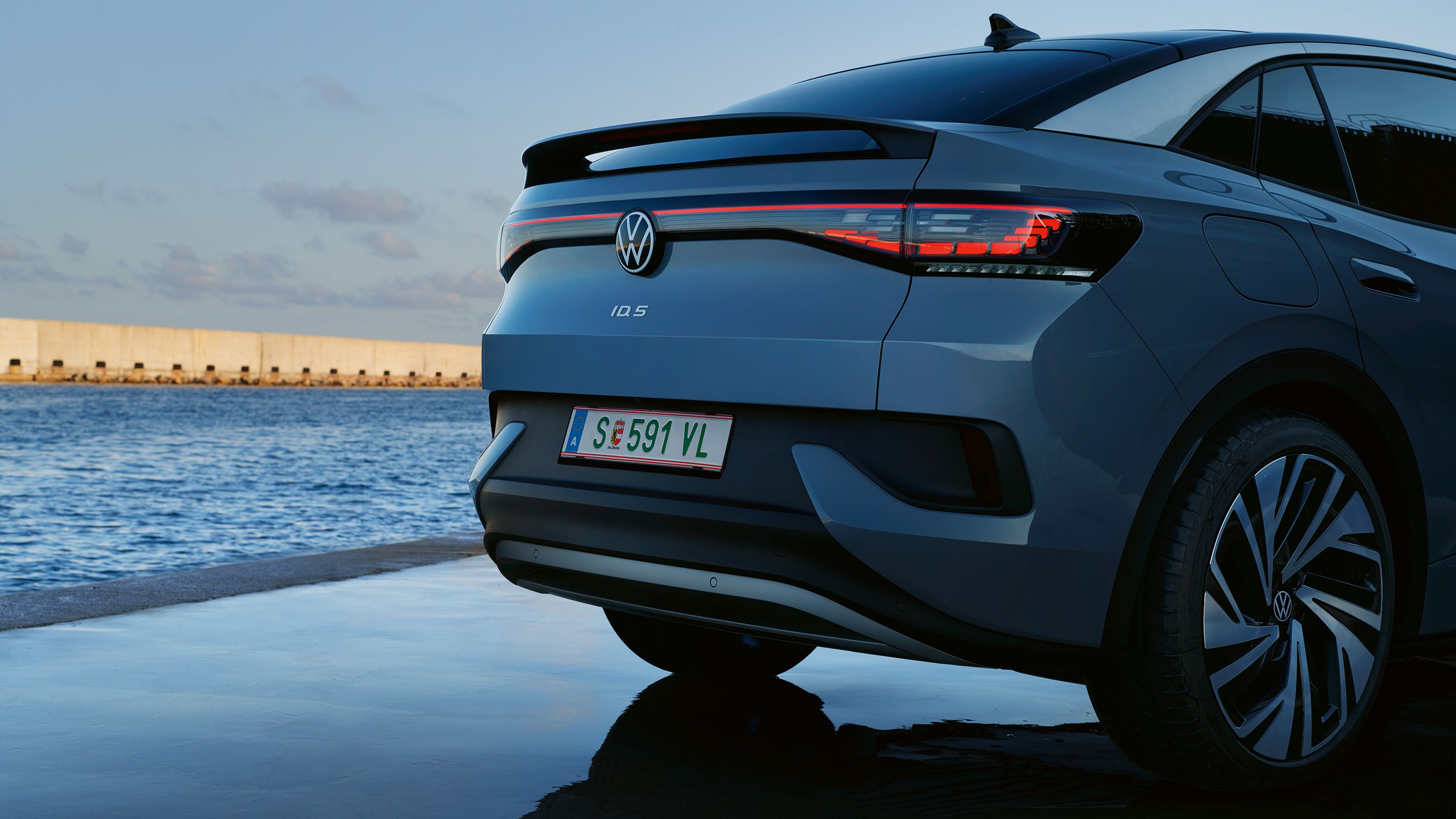 Heck eines stehenden VW ID.5, Abendstimmung am Meer, eingeschaltete LED-Rückleuchten