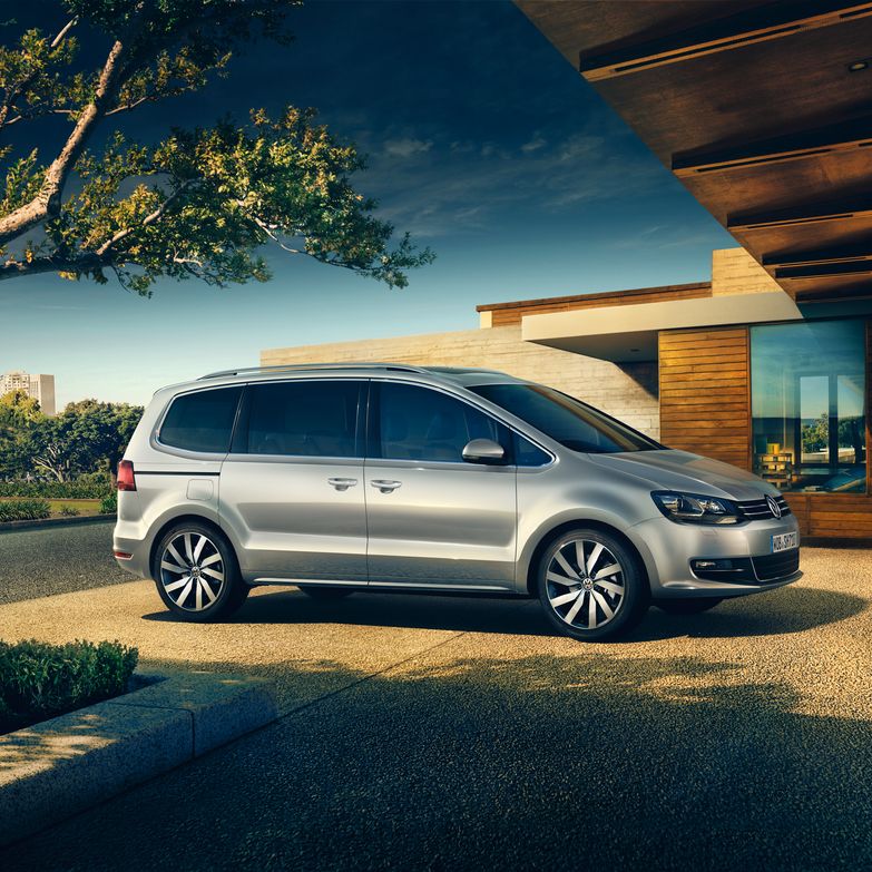 Сребрист Volkswagen Sharan, паркиран в двора на съвременна къща с панорамна гледка към града.