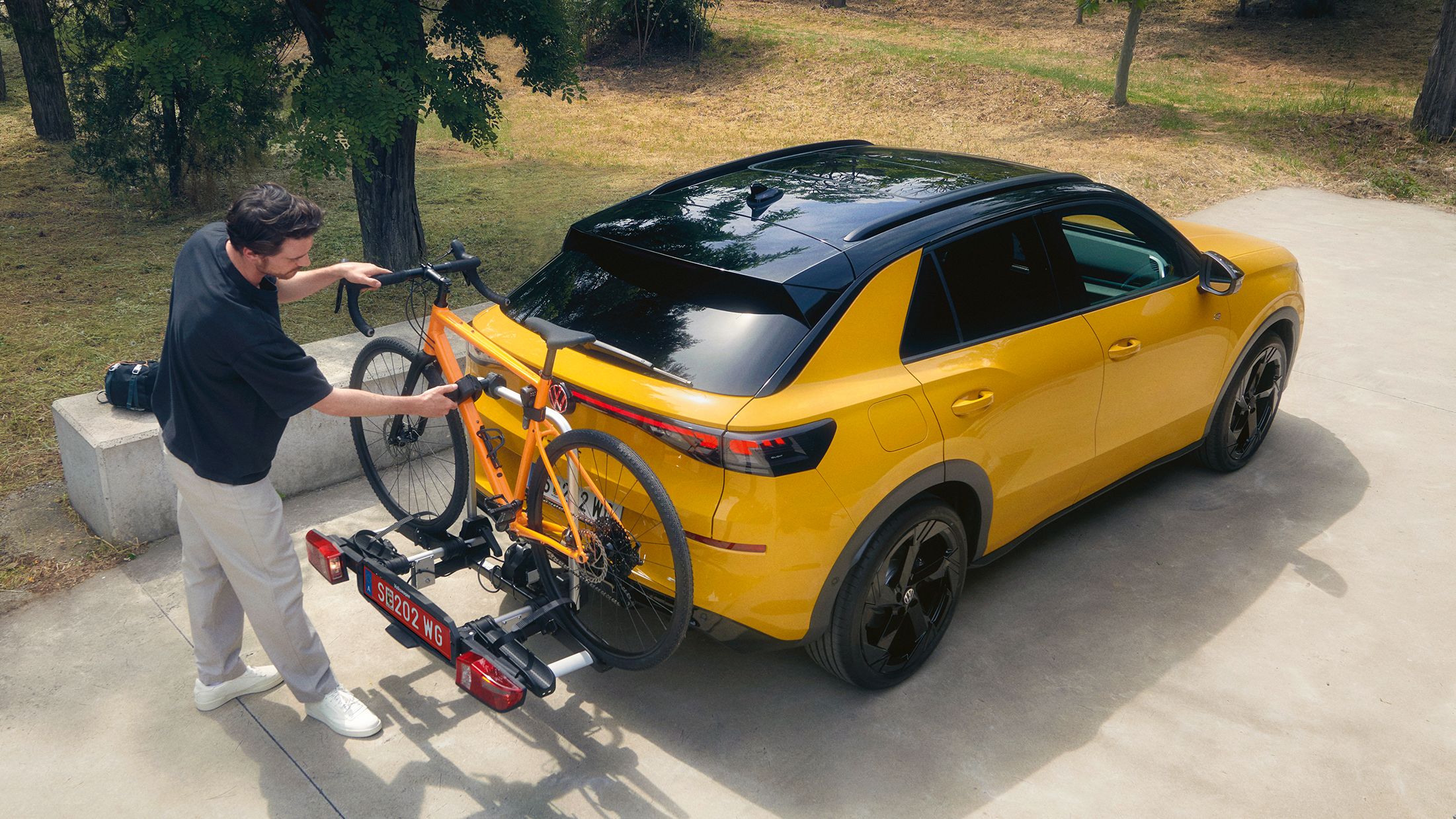 Мъж закрепя велосипед на багажник за колела върху жълт Volkswagen T-Roc.