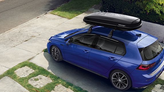 Ein blauer VW Golf mit Dachbox parkt vor einer Hauseinfahrt