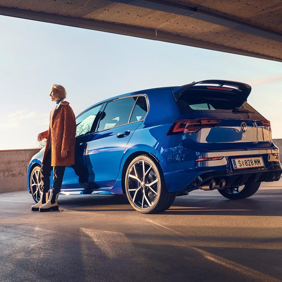 Син Volkswagen Golf R, заснет отзад с човек до него на открит паркинг при залез