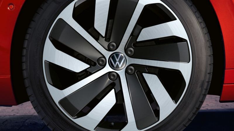Близък план на сребриста алуминиева джанта с емблема Volkswagen на червен Arteon Shooting Brake