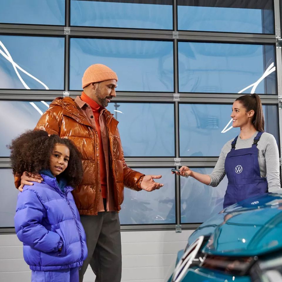 Eine VW Service Technikerin übergibt die Fahrzeugschlüssel an einen Mann mit Kind
