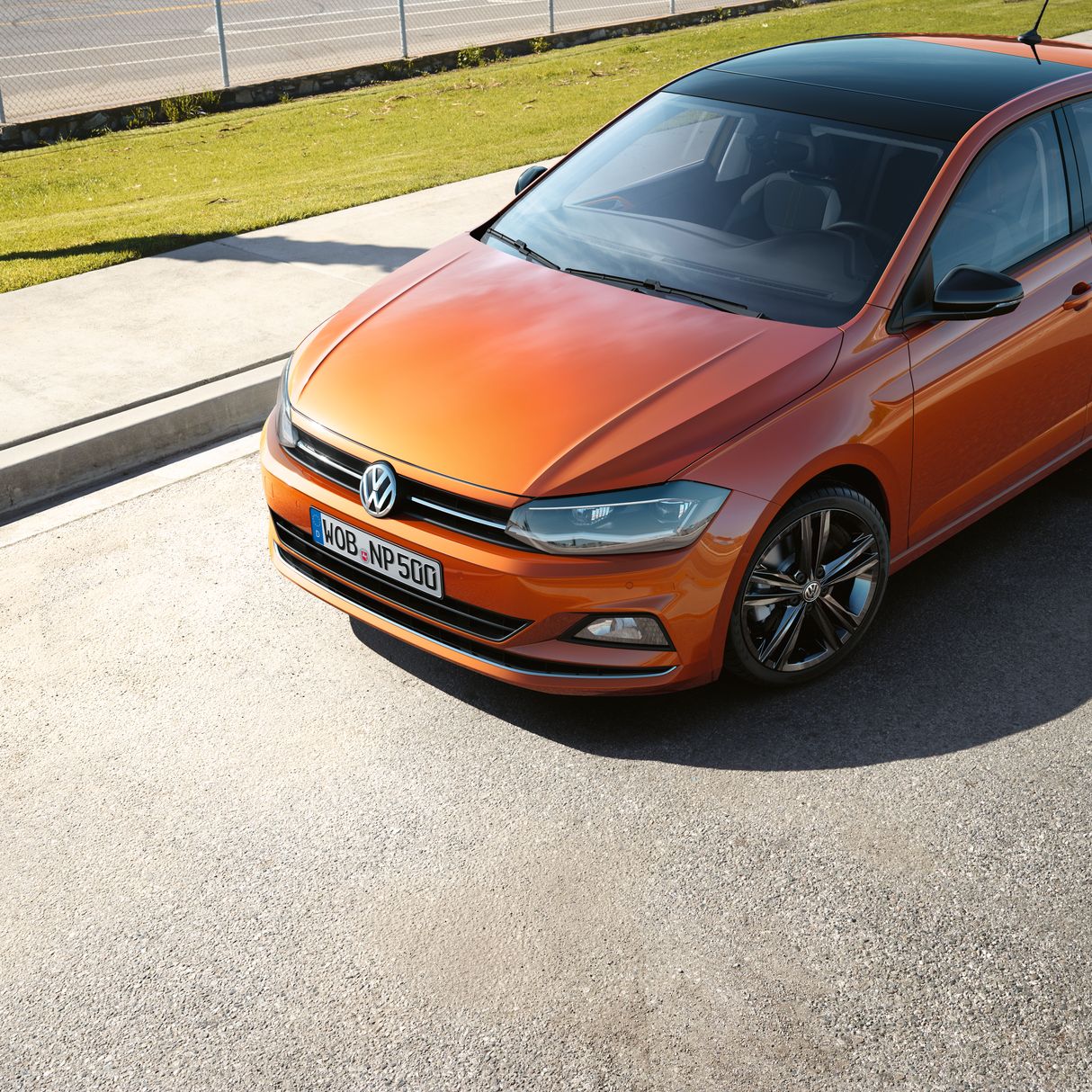 Оранжев Volkswagen Polo с черен покрив, паркиран на слънчев път
