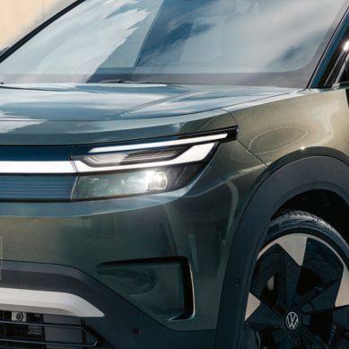 Зелен VW ID. Cross стои пред модерна стъклена сграда върху бетонна повърхност.