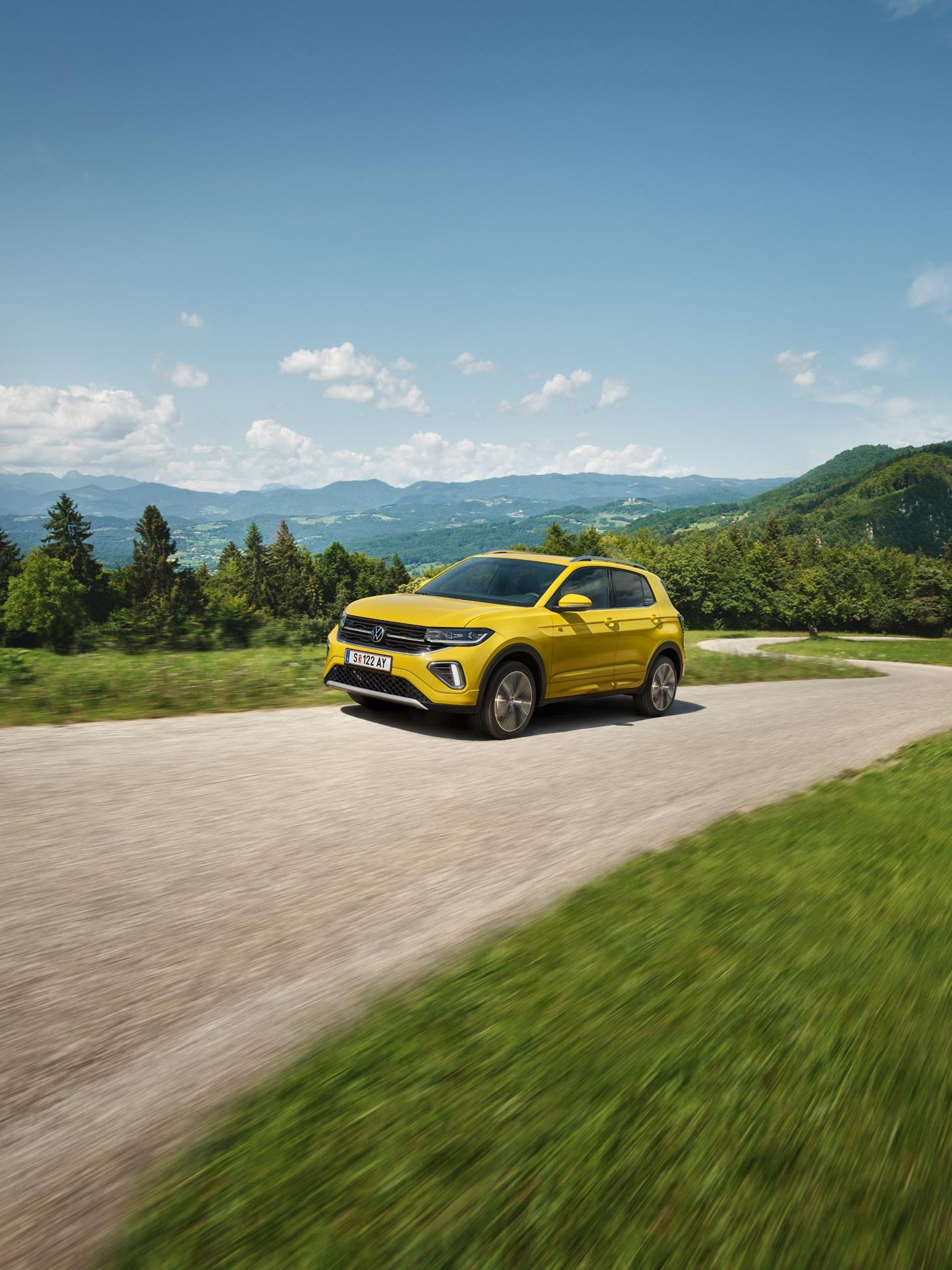 Жълт VW T-Cross на път сред хълмист пейзаж.