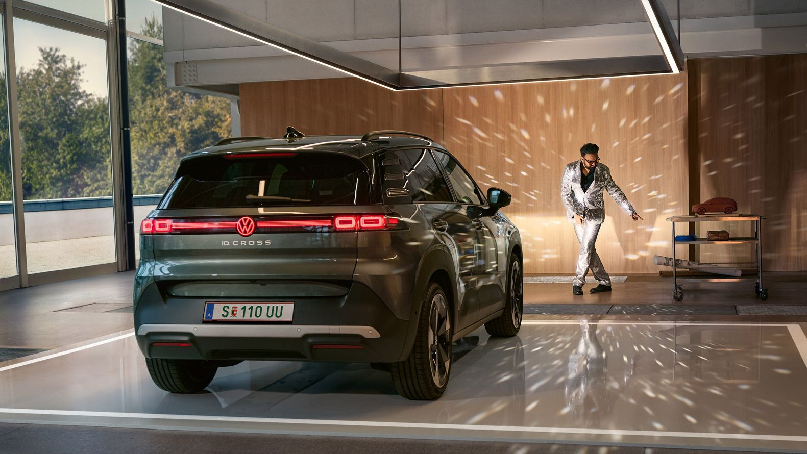 VW ID. Cross стои в коридор с включени фарове и осветява танцуващ мъж в блестящ костюм.