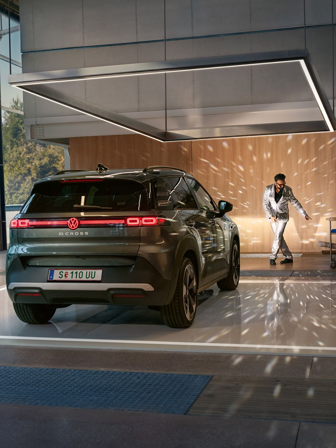 VW ID. Cross стои в коридор с включени фарове и осветява танцуващ мъж в блестящ костюм.