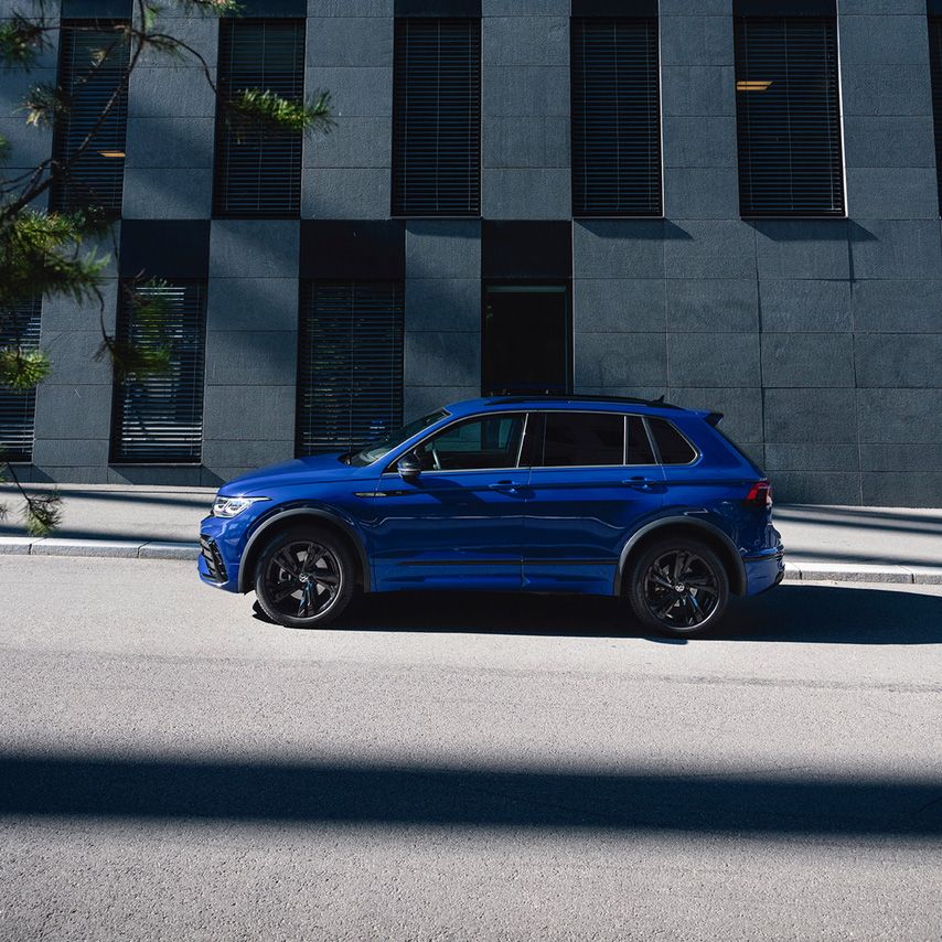 Син Volkswagen Tiguan R, заснет в профил, паркиран на улица до фасада на съвременна офис сграда