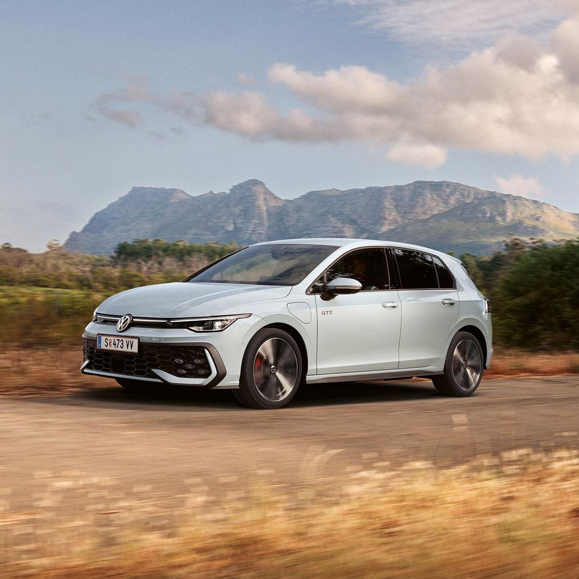 Volkswagen Golf GTE в движение по живописен път с планински пейзаж