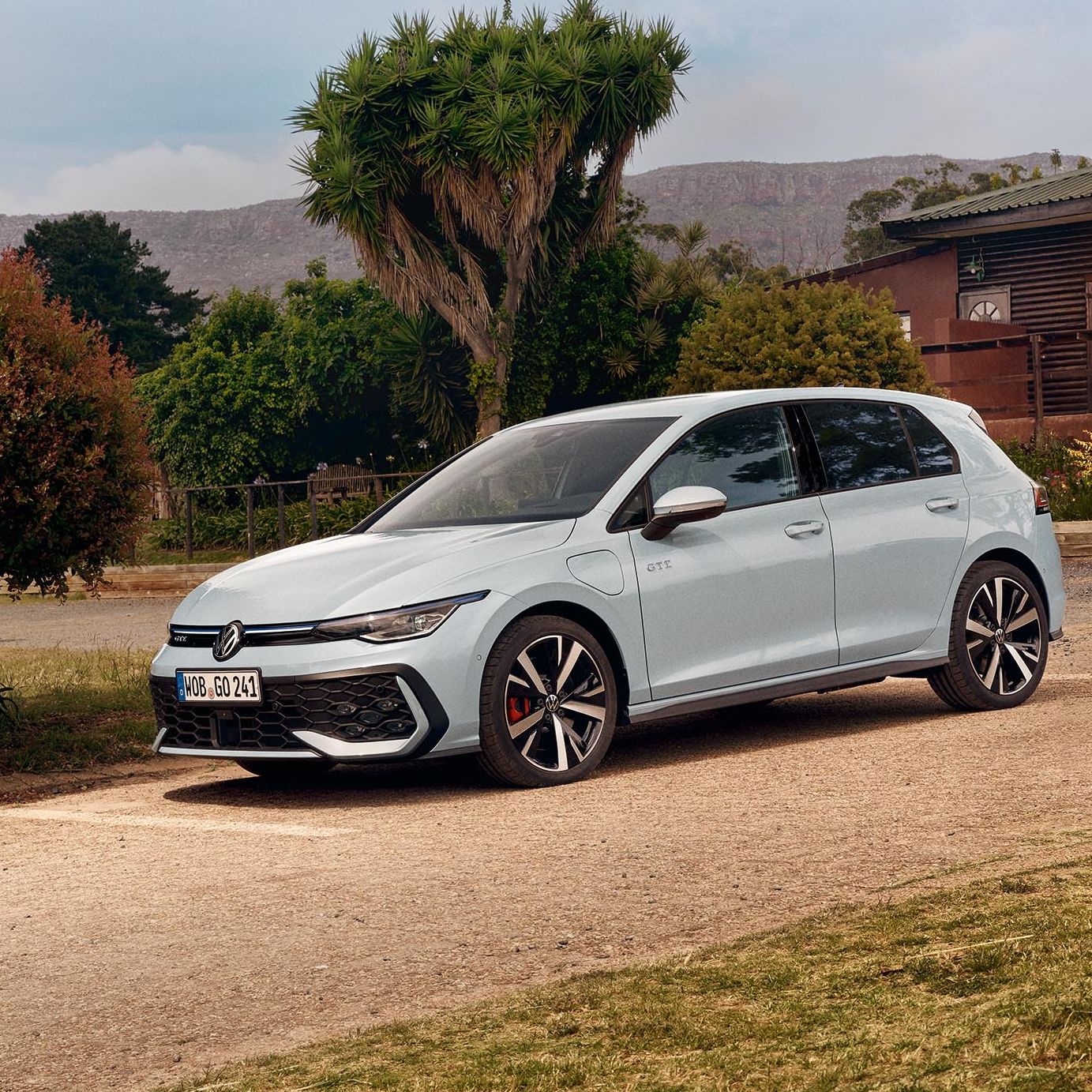 Бял Volkswagen Golf, паркиран до къща с градина, докато баща и дъщеря се забавляват навън