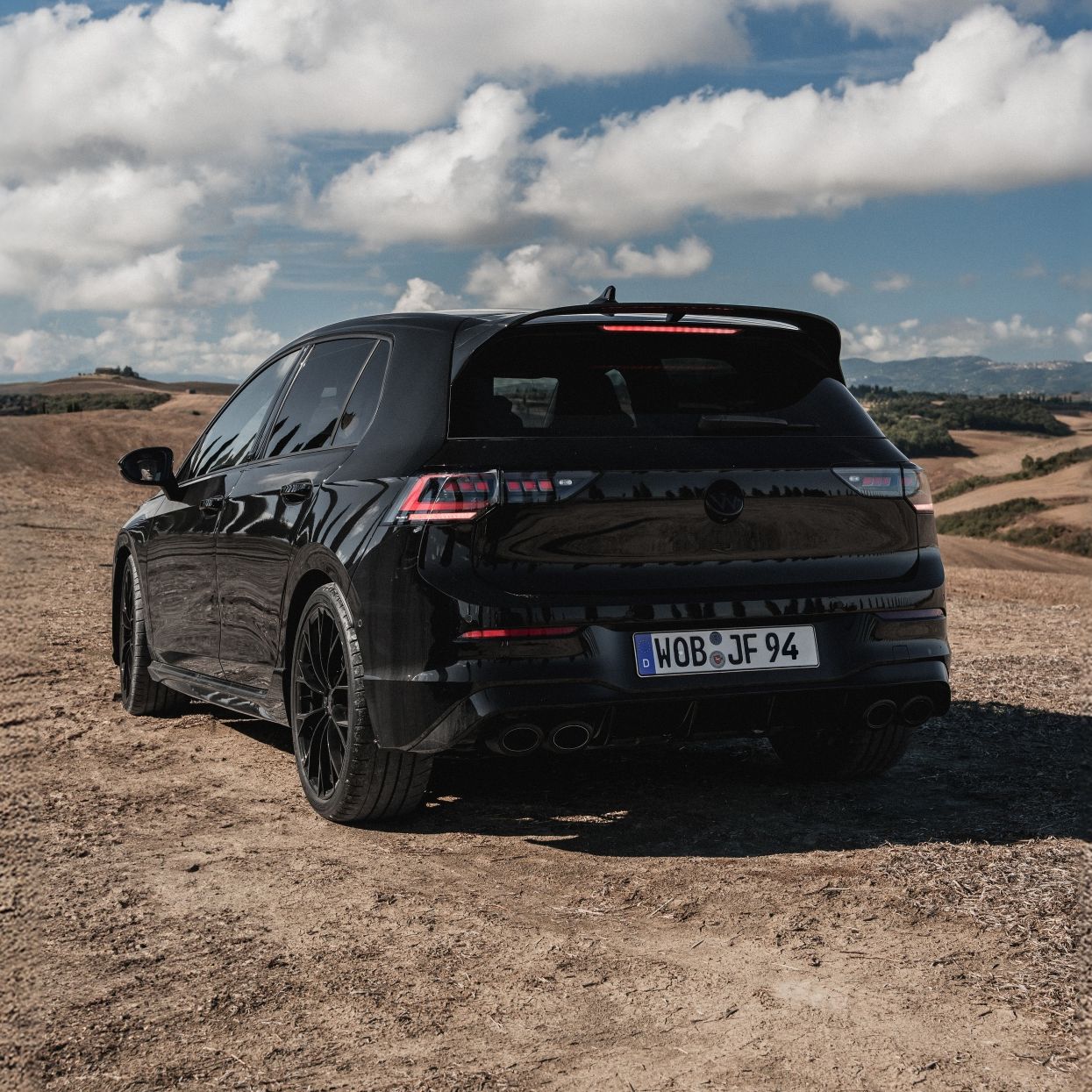 Черен Volkswagen Golf R, заснет отзад сред живописен пейзаж с хълмове и синьо небе