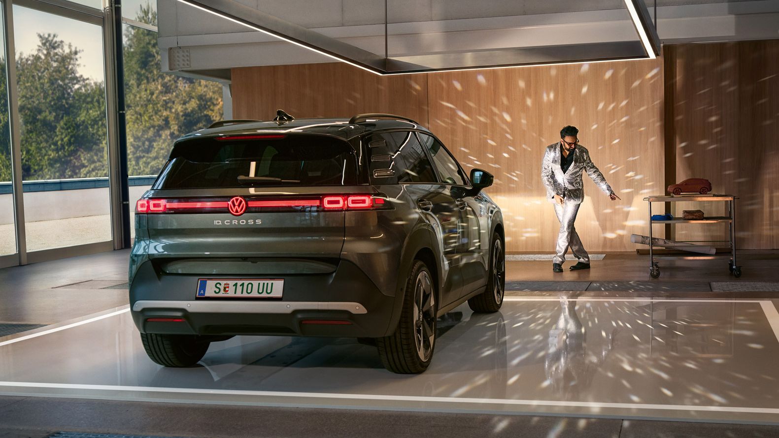 VW ID. Cross стои в коридор с включени фарове и осветява танцуващ мъж в блестящ костюм.