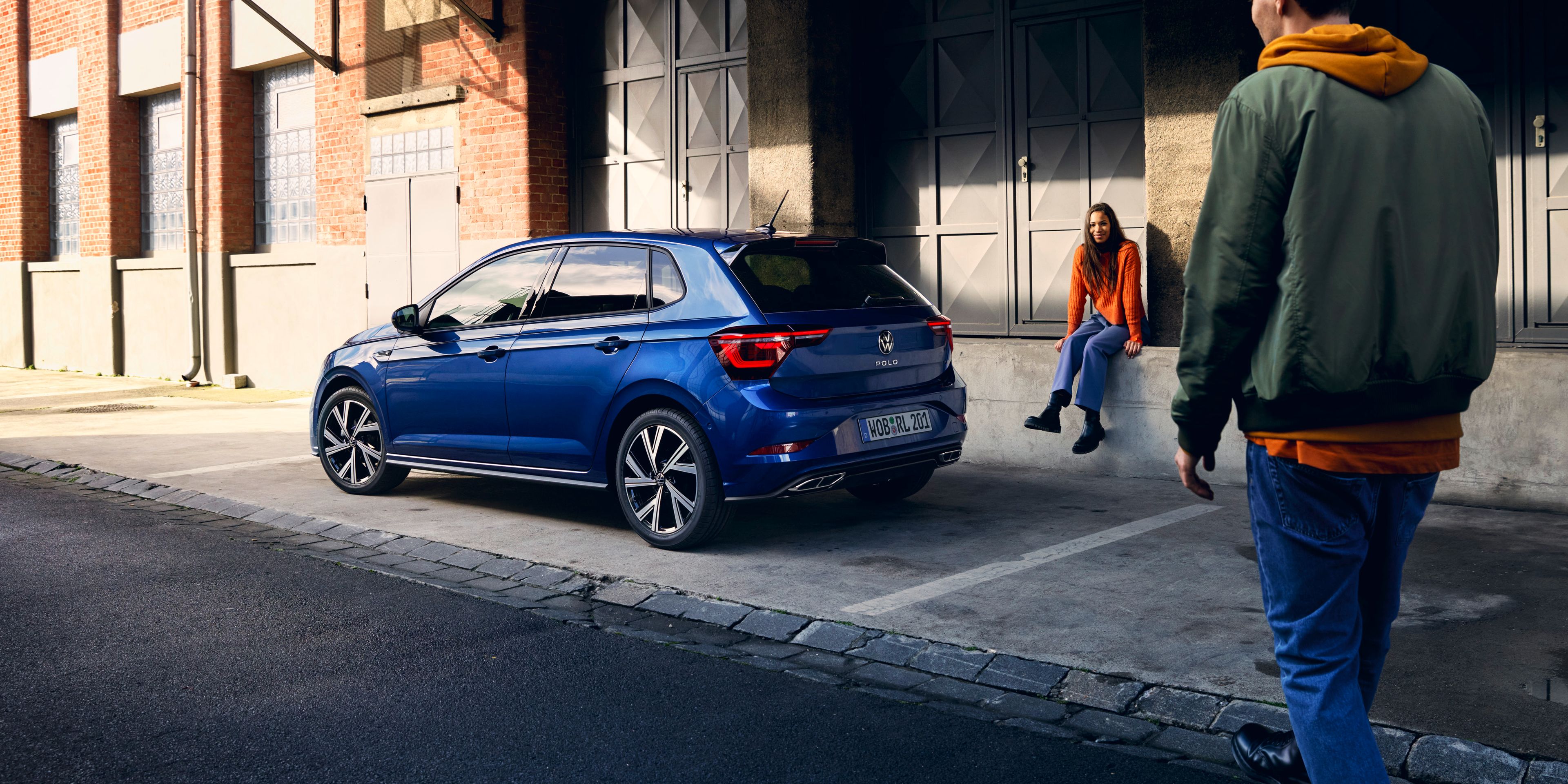 Ein blauer VW Polo steht vor einer Rampe, ein Mann geht am Heck mit den optionalen LED-Rückleuchten vorbei. 