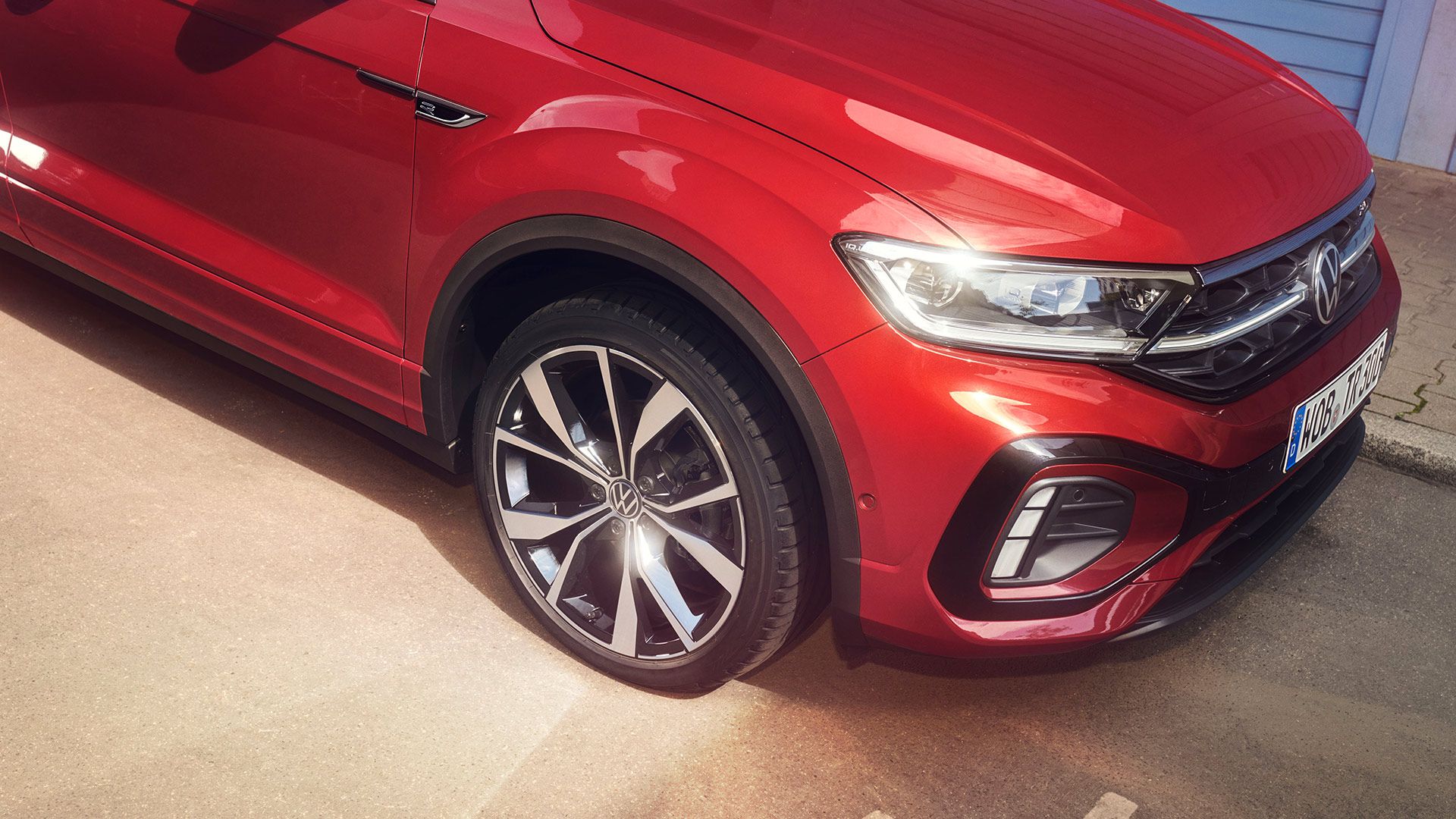 Страничен поглед към предната част на T-Roc Cabriolet в червен цвят с поглед към колелата и светлините. 