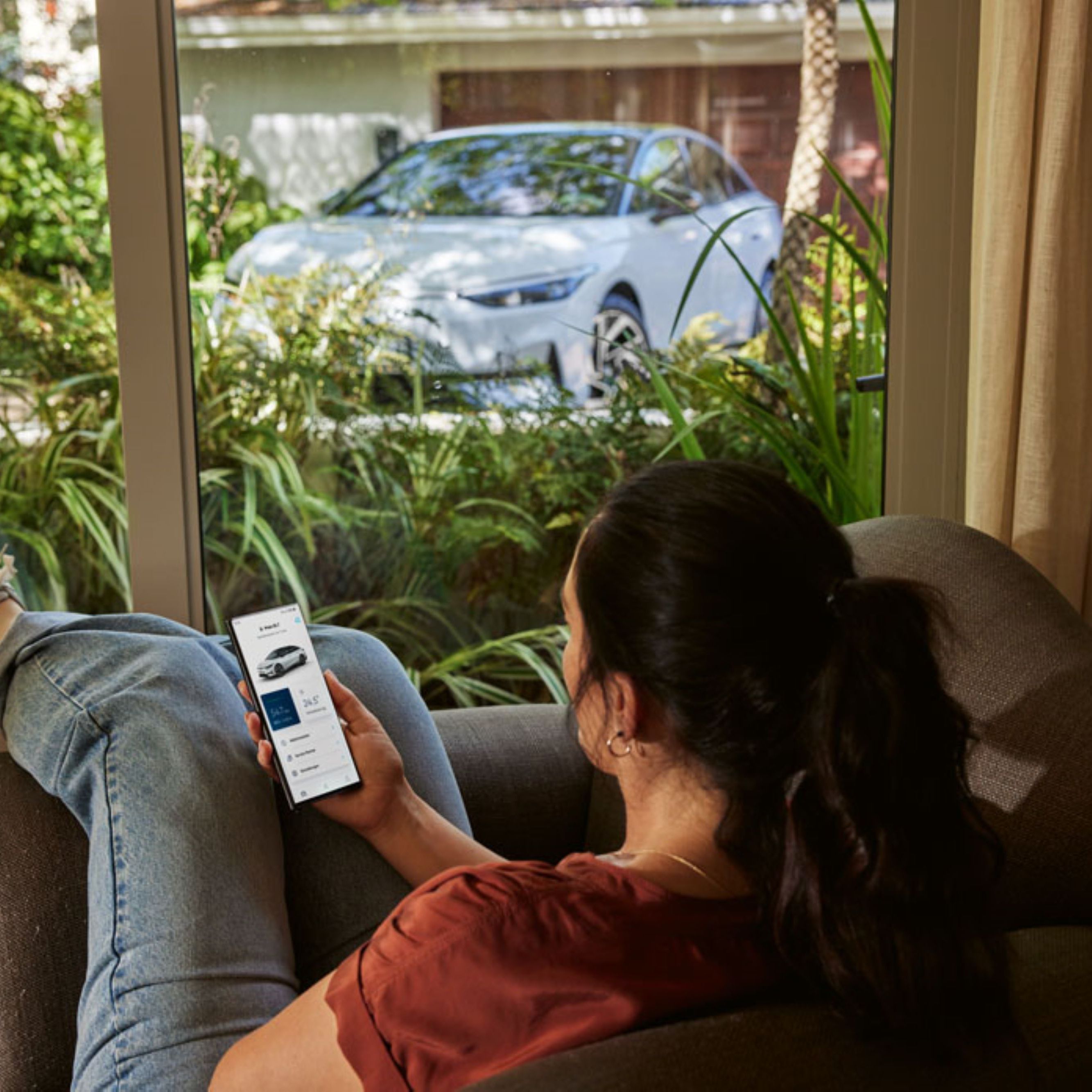 Person liegt auf Couch mit Smartphone in der Handy und schaut sich ein Auto an.