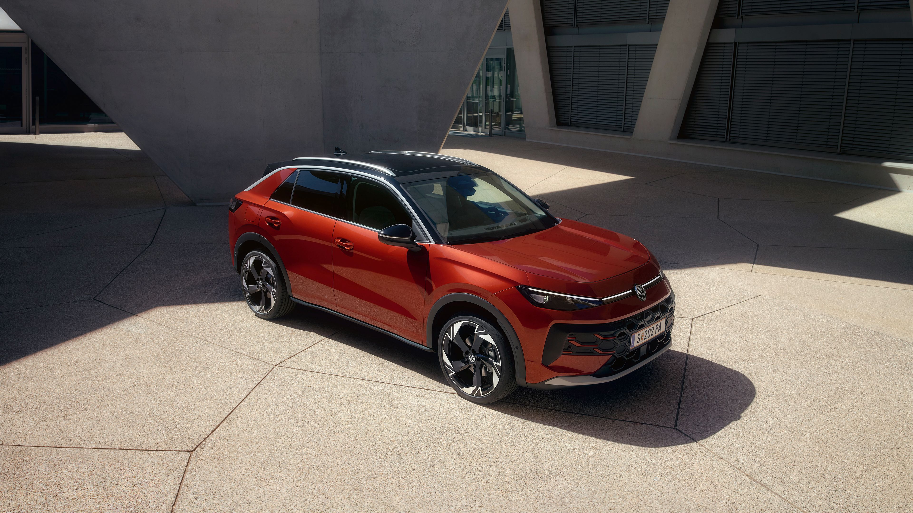 Червен Volkswagen T-Roc паркиран пред модерна сграда с геометричен дизайн.