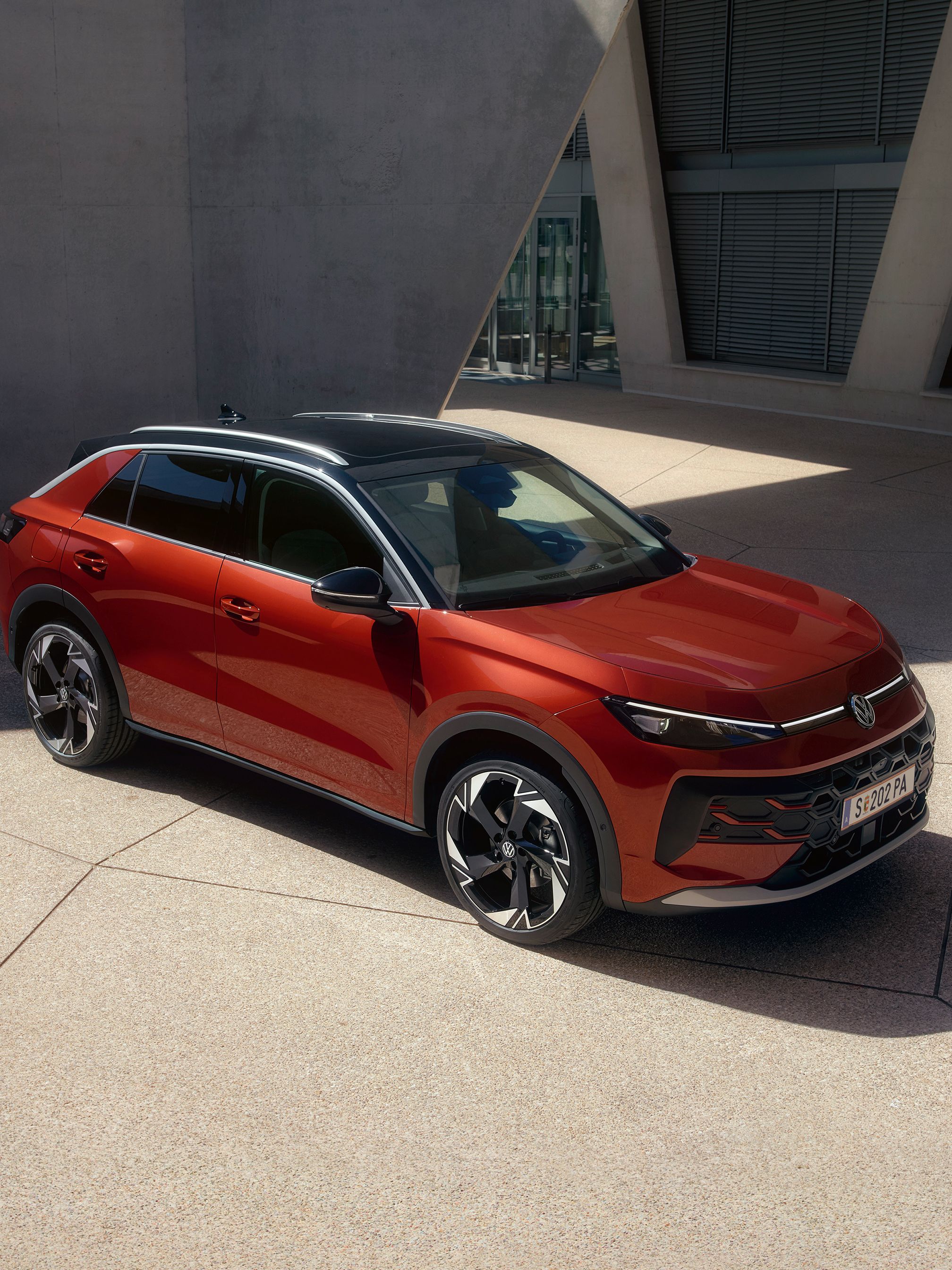 Червен Volkswagen T-Roc паркиран пред модерна сграда с геометричен дизайн.