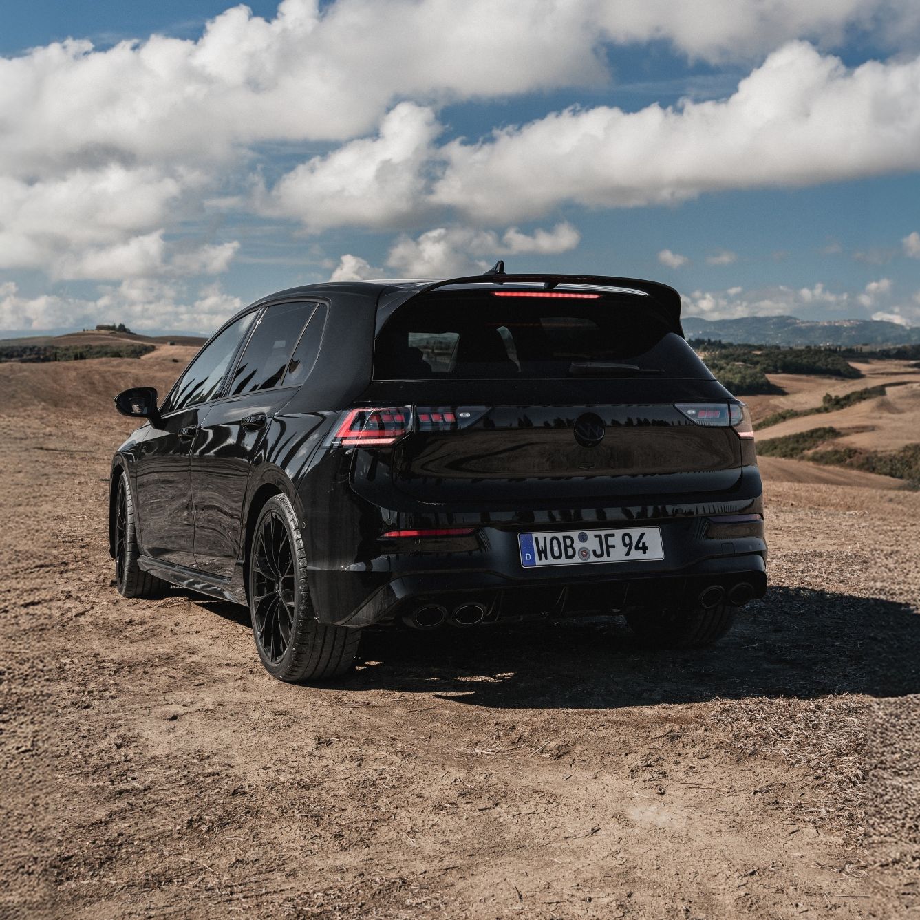 Черен Volkswagen Golf R, заснет отзад сред живописен пейзаж с хълмове и синьо небе