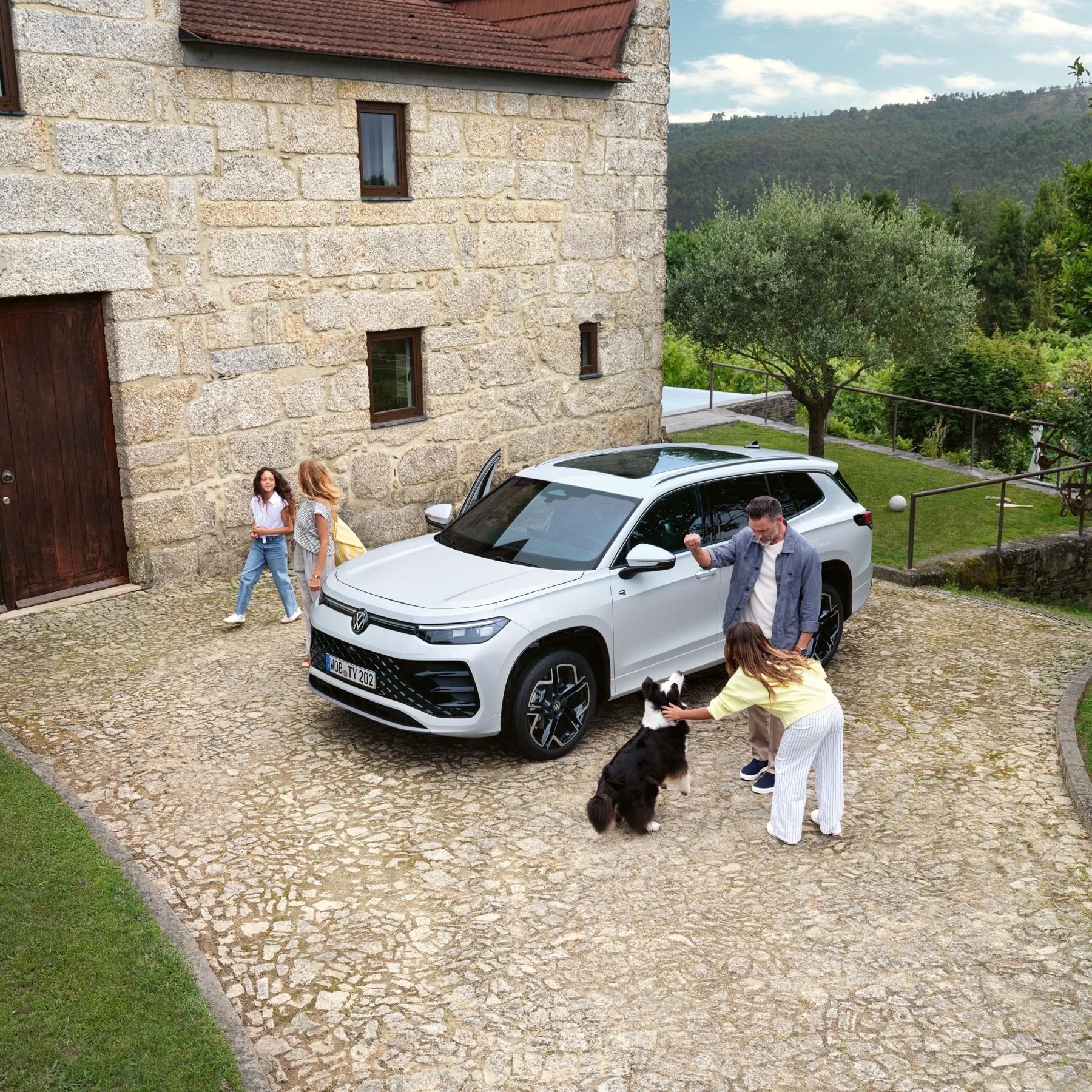 Семейство с куче пред къща до паркиран бял Volkswagen Tayron