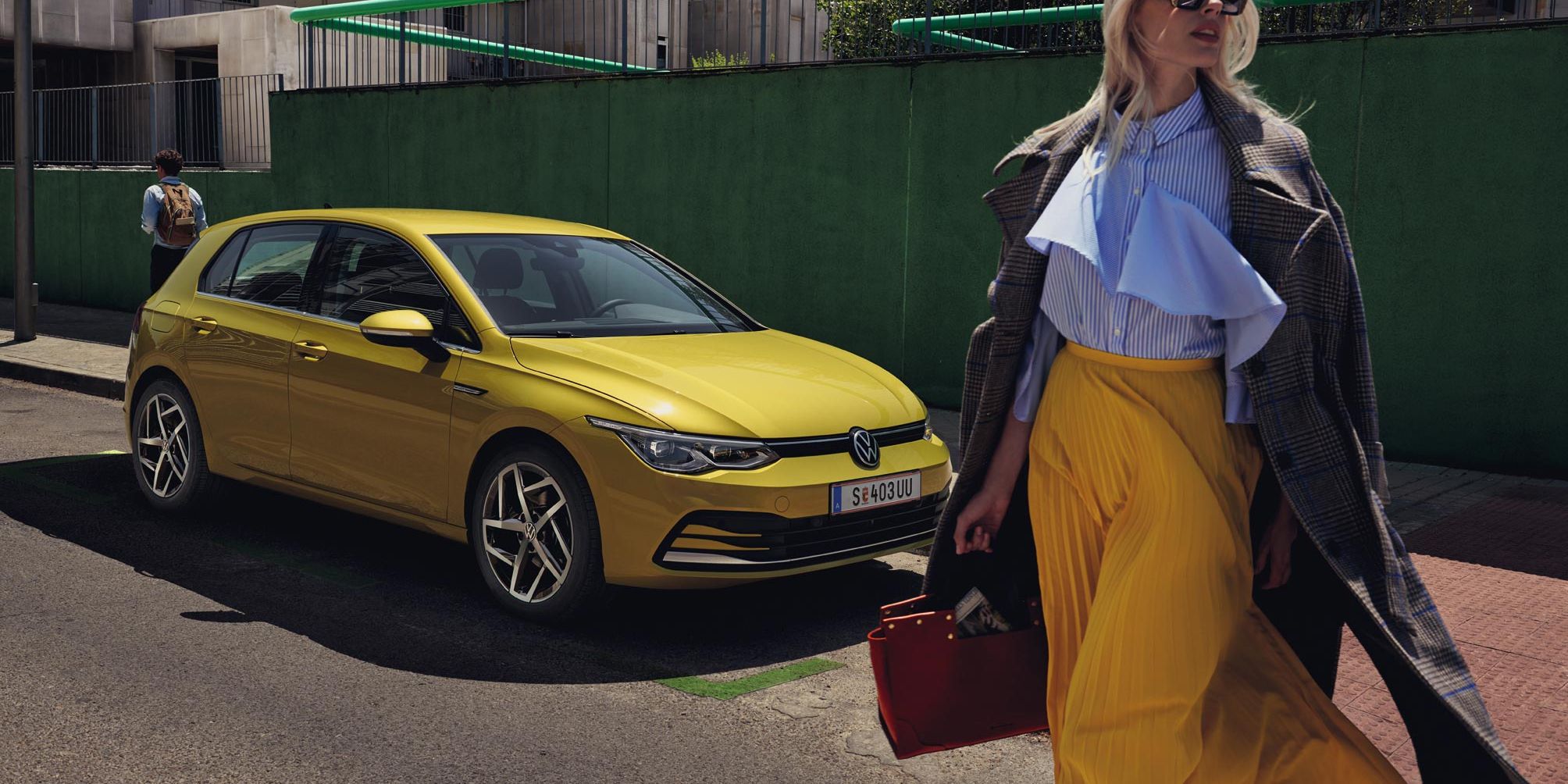 Жълт Volkswagen Golf паркиран на градска улица с модерно облечена жена на преден план
