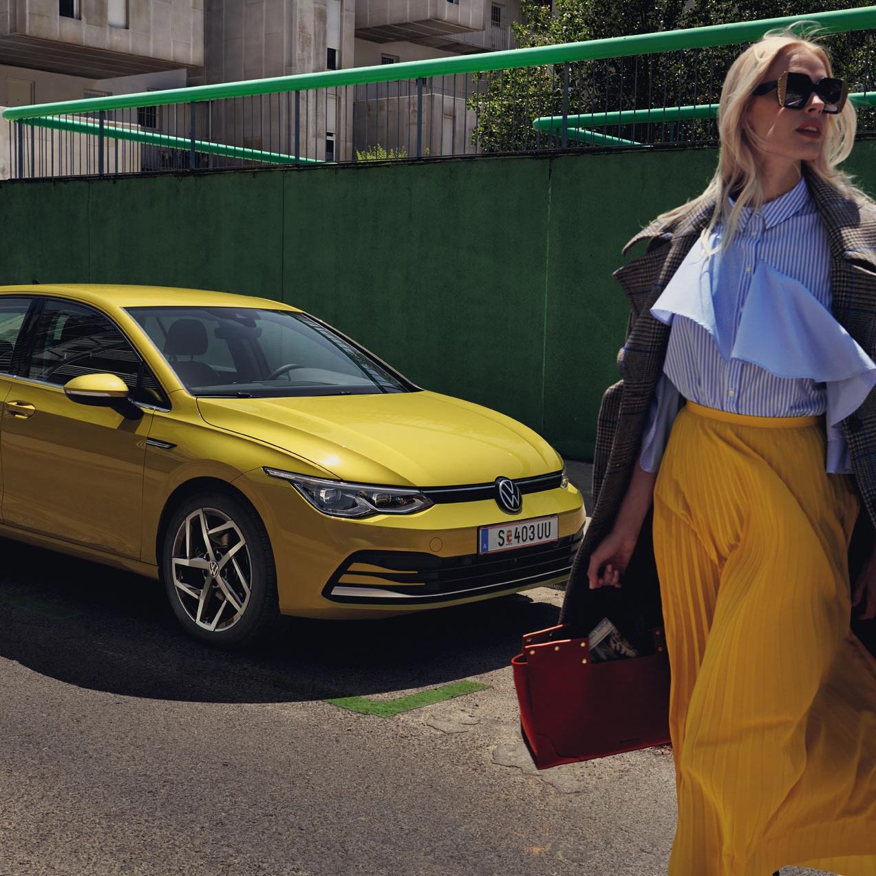 Жълт Volkswagen Golf паркиран на градска улица с модерно облечена жена на преден план