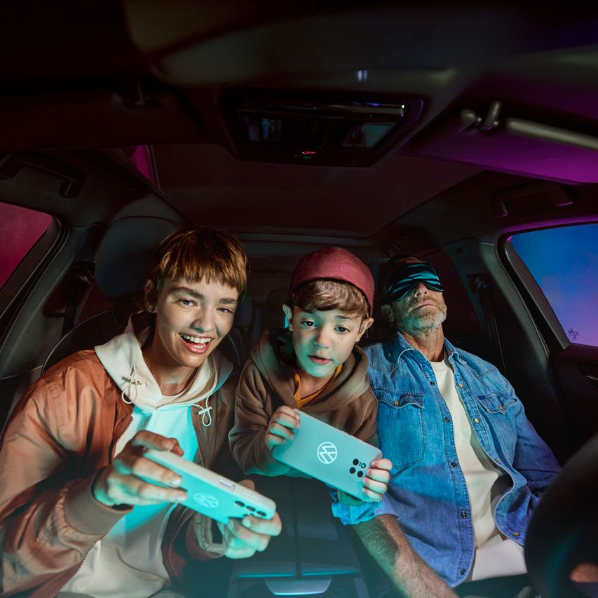 Vater mit zwei Kindern im Volkswagen, die Kinder spielen mit der AirConsole.