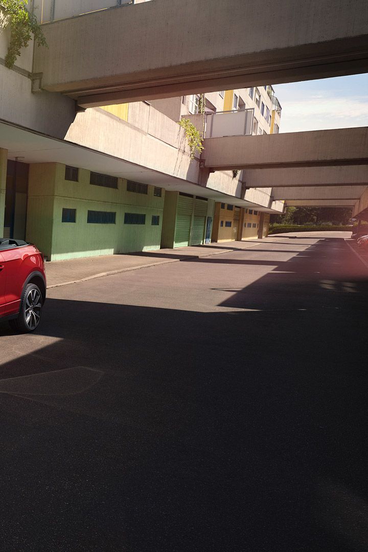 Rotes VW T-Roc Cabriolet mit geöffnetem Dach parkt am Straßenrand. Eine Frau mit zwei Hunden steht daneben. 