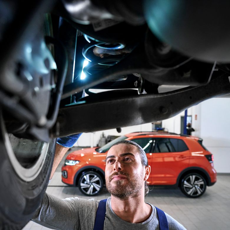 Техник на Volkswagen извършва инспекция под автомобила в сервиза.