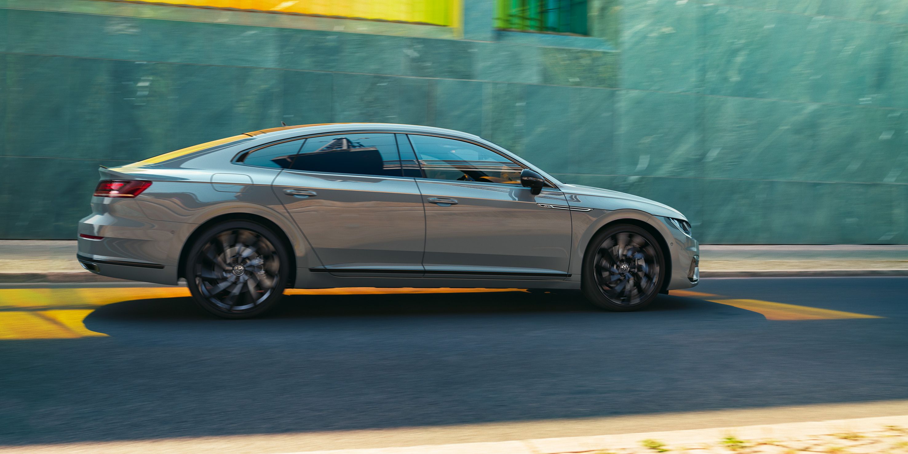 Сив Volkswagen Arteon Shooting Brake се движи по градска улица пред модерна стъклена фасада