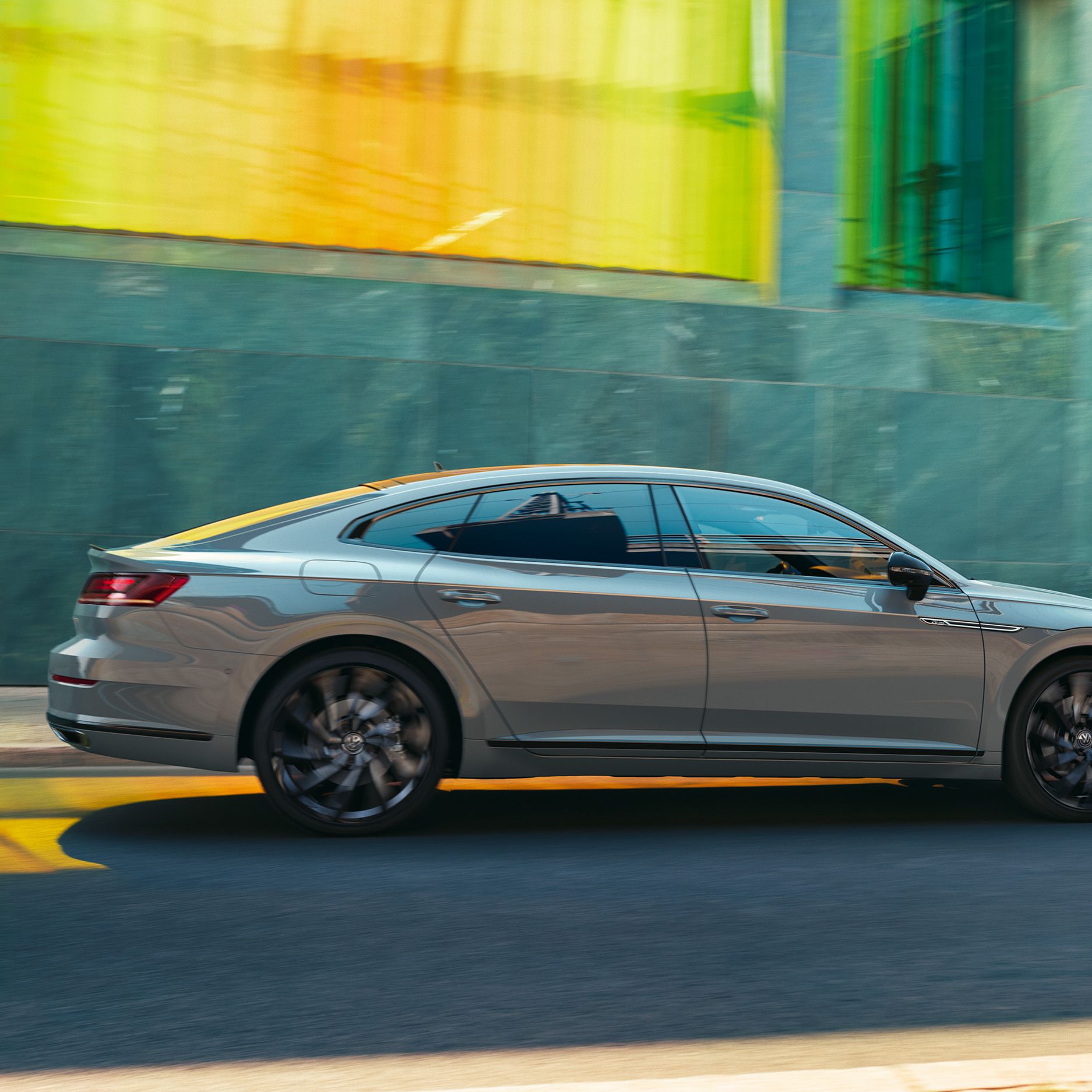 Сив Volkswagen Arteon Shooting Brake се движи по градска улица пред модерна стъклена фасада