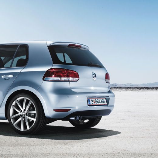Задно-страничен изглед на светлосин Volkswagen Golf VII, паркиран върху открито сухо пространство под синьо небе