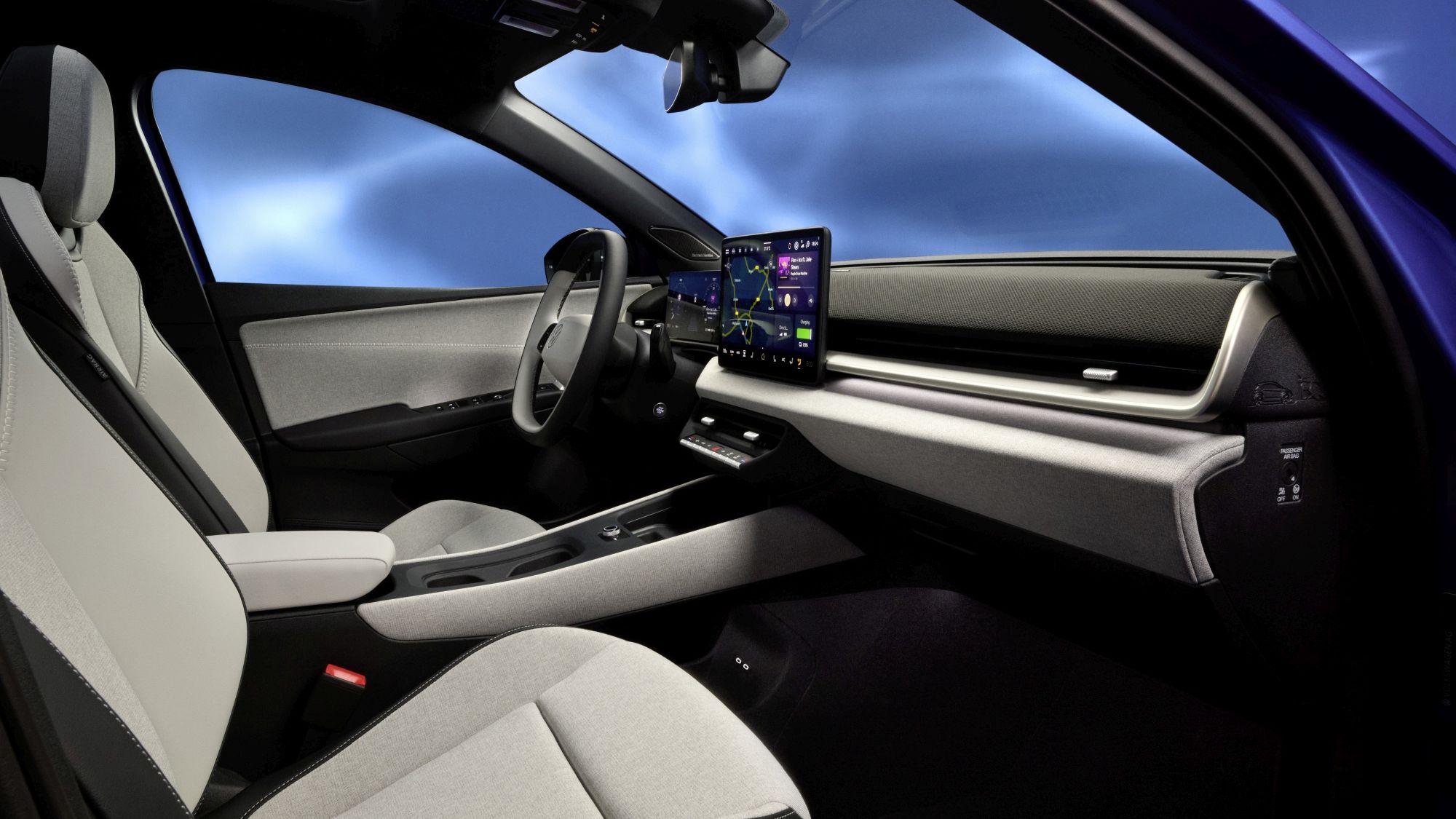 Интериор на съвременен автомобил Polo с две предни седалки в сиви и бели тонове. На таблото е разположен голям сензорен екран с навигация и различни икони. Прозорецът показва синьо небе с облаци.