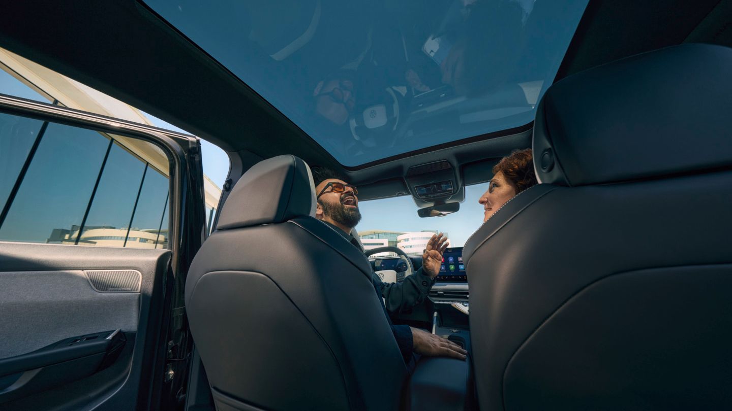 Усмихнат мъж седи на шофьорската седалка на VW ID. Cross и гледа през отворения панорамен покрив.