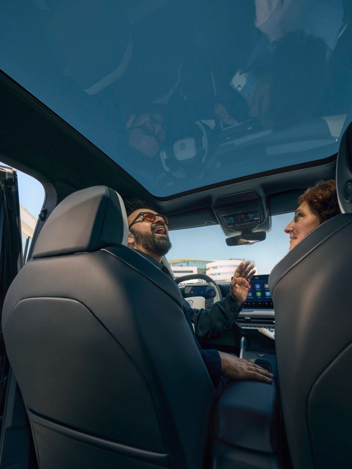 Усмихнат мъж седи на шофьорската седалка на VW ID. Cross и гледа през отворения панорамен покрив.