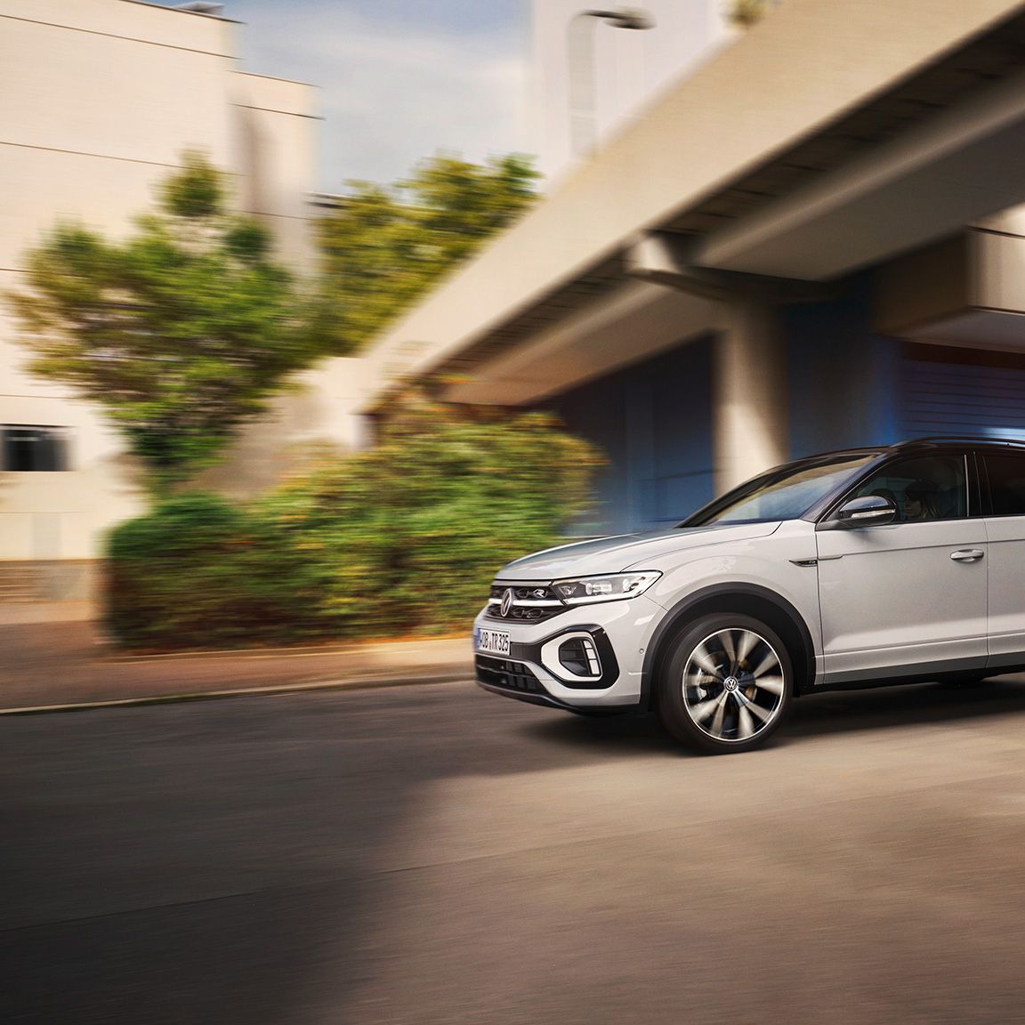 VW T-Roc R-Line in weiß fährt dynamisch über Kreuzung, von der Seite zu sehen