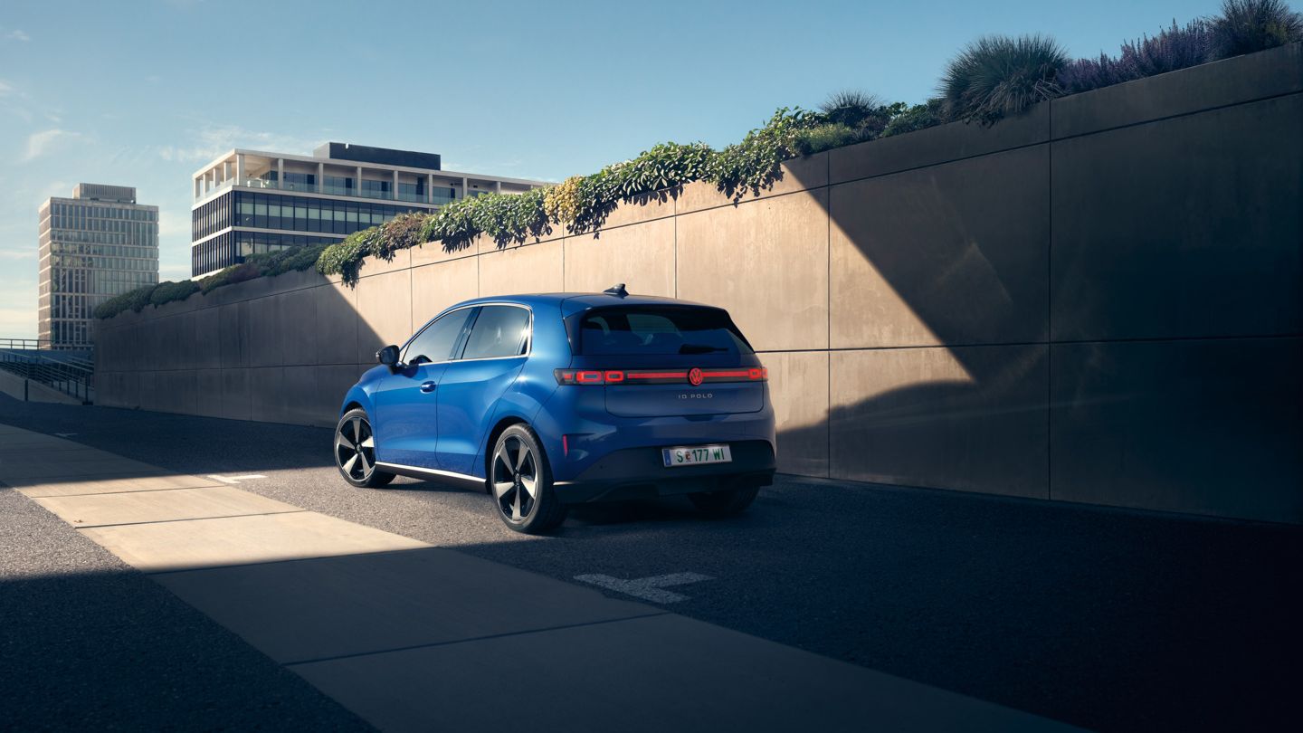 Син VW ID. Polo Style стои край пътя пред зелена стена.