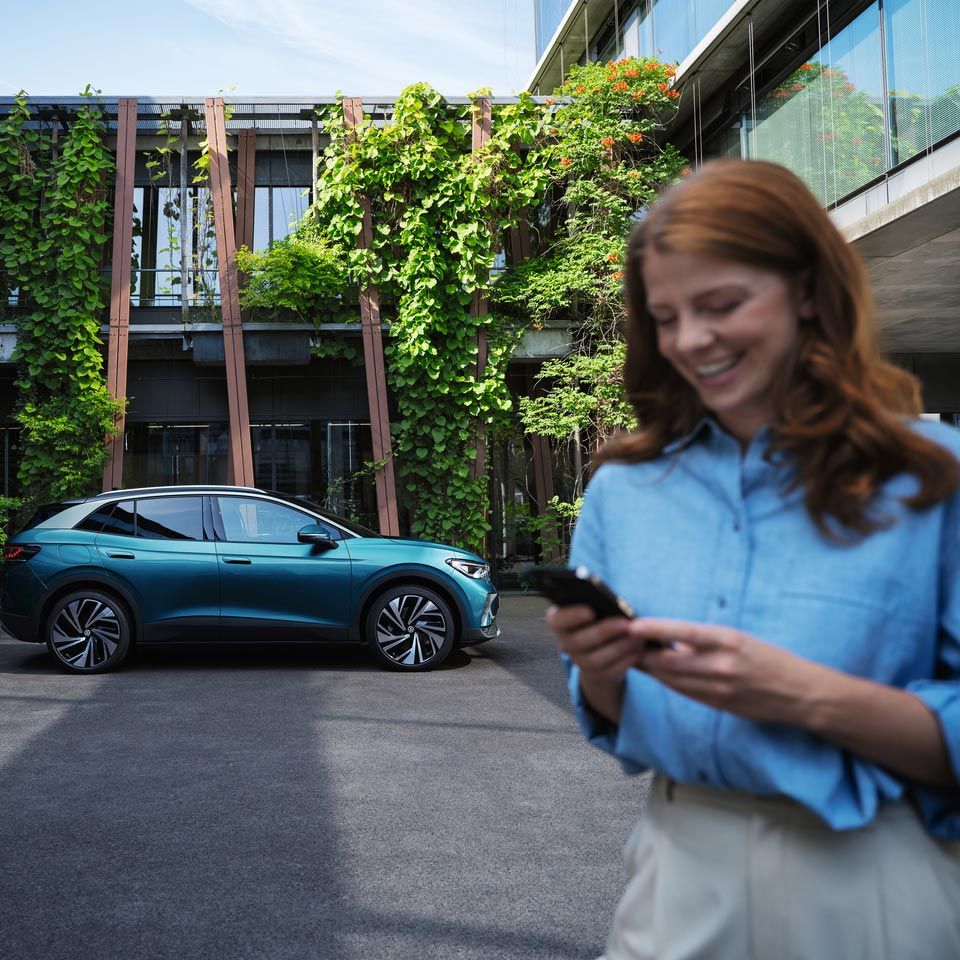 Junge Frau steht im Hof vor einem VW ID.4 Pro. Sie hält ein Handy in der Hand.