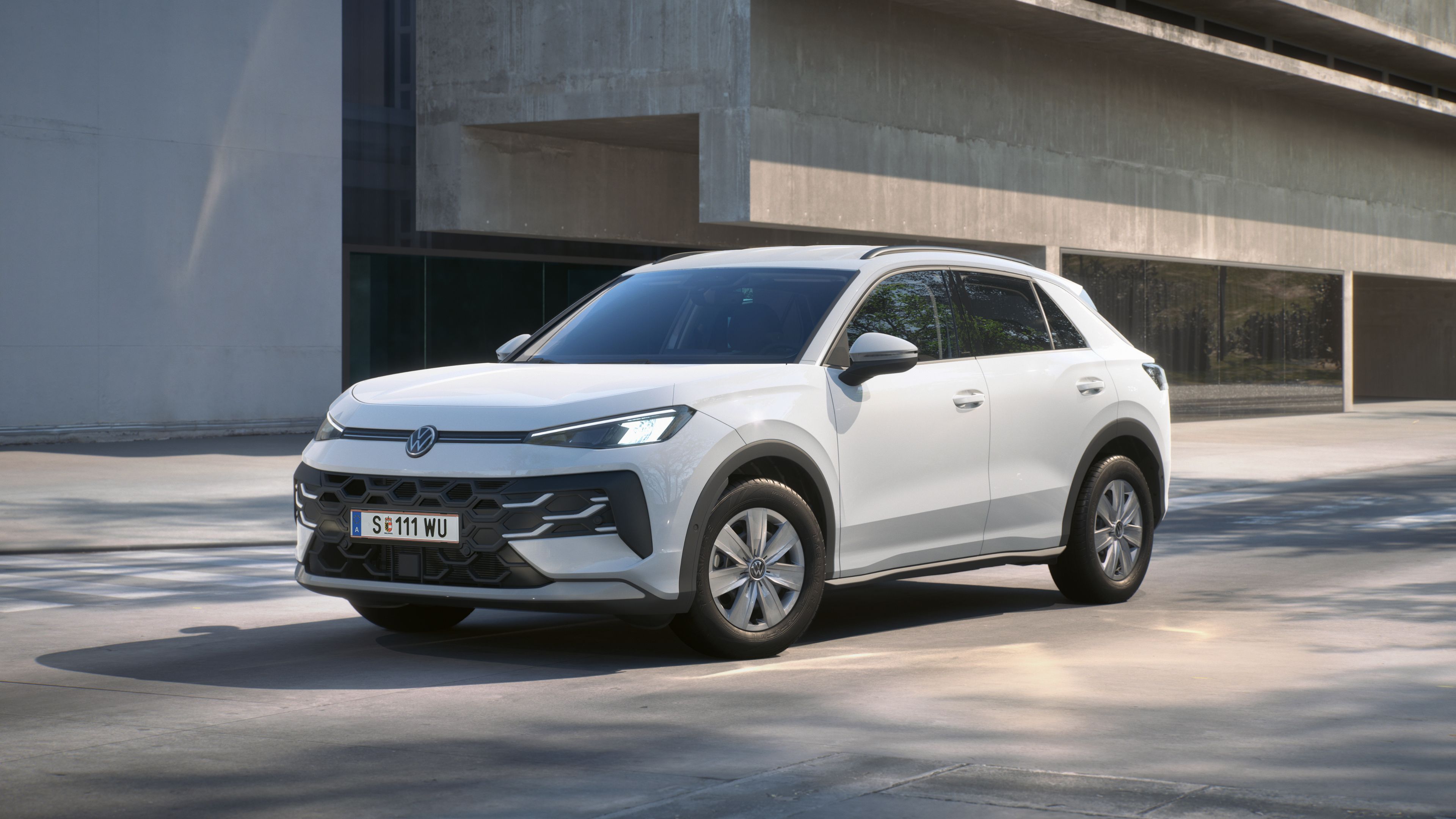Бял Volkswagen T-Roc, заснет отпред под ъгъл пред модерна сграда.