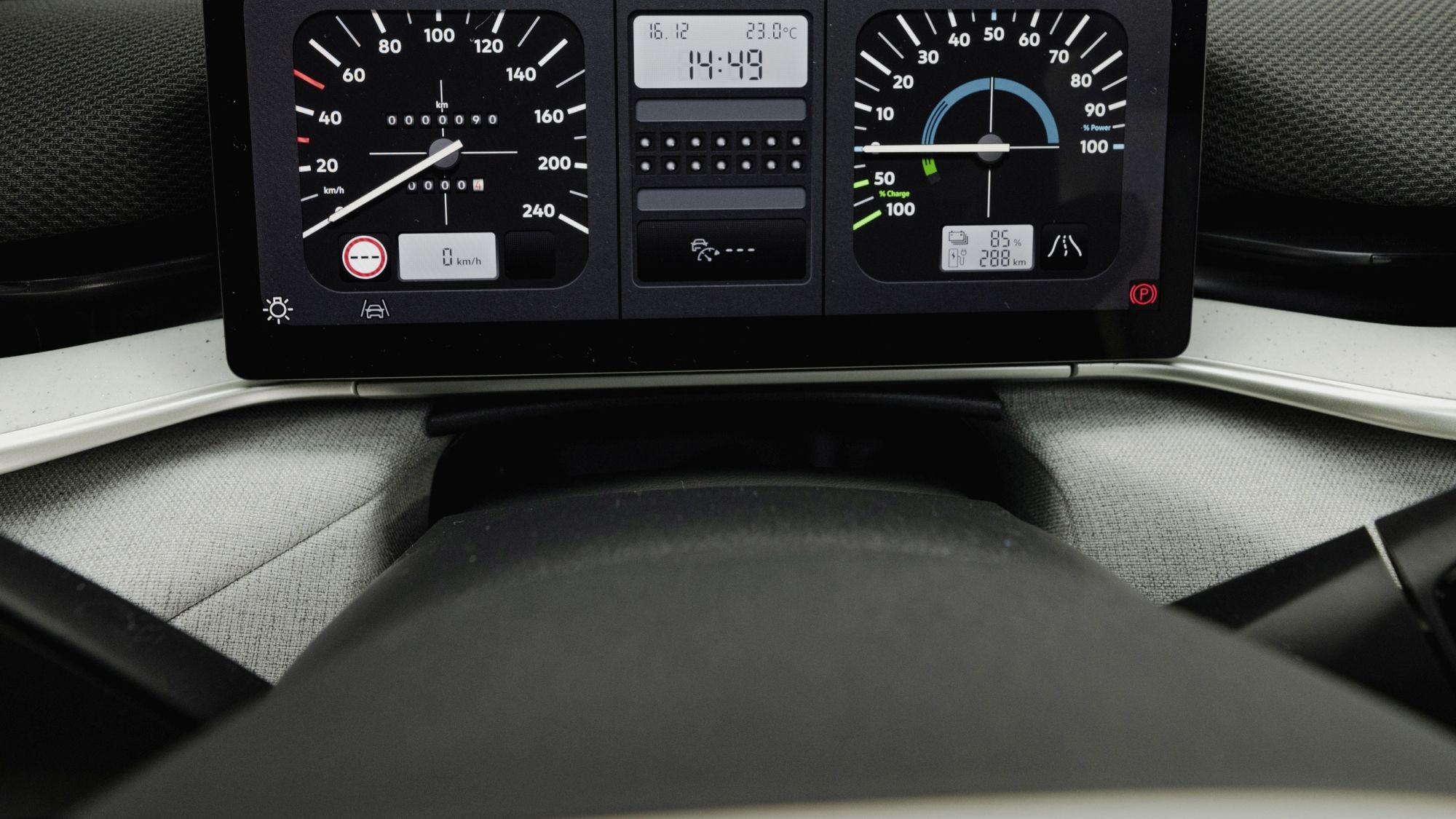 Изображението показва приборното табло на автомобил с два аналогови скоростомера и цифров дисплей, показващ час. Таблото е модерно и има различни индикатори за състоянието на автомобила. Небето се вижда през предното стъкло.