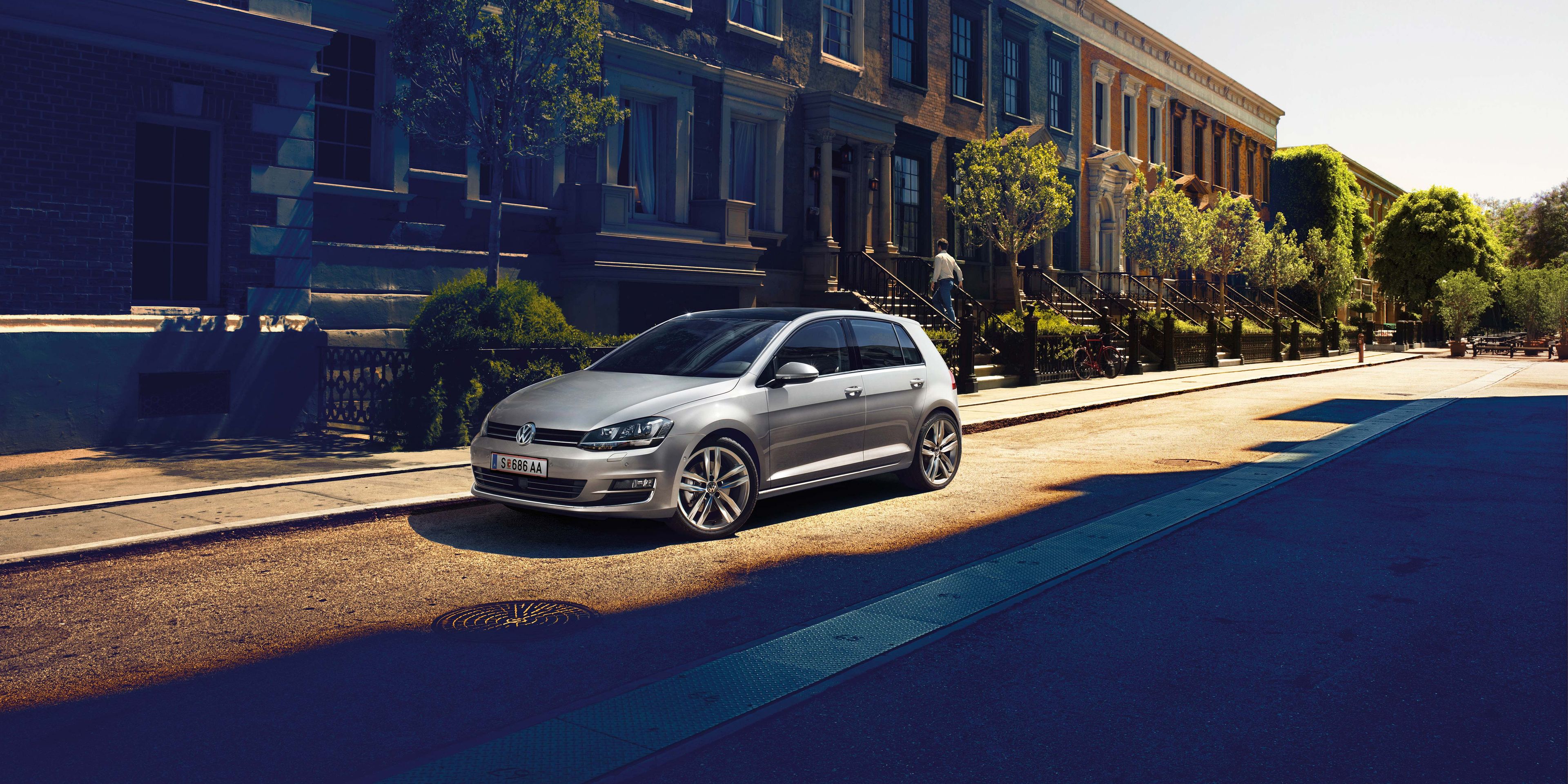 Сребрист Volkswagen Golf, паркиран на улица в слънчев градски район