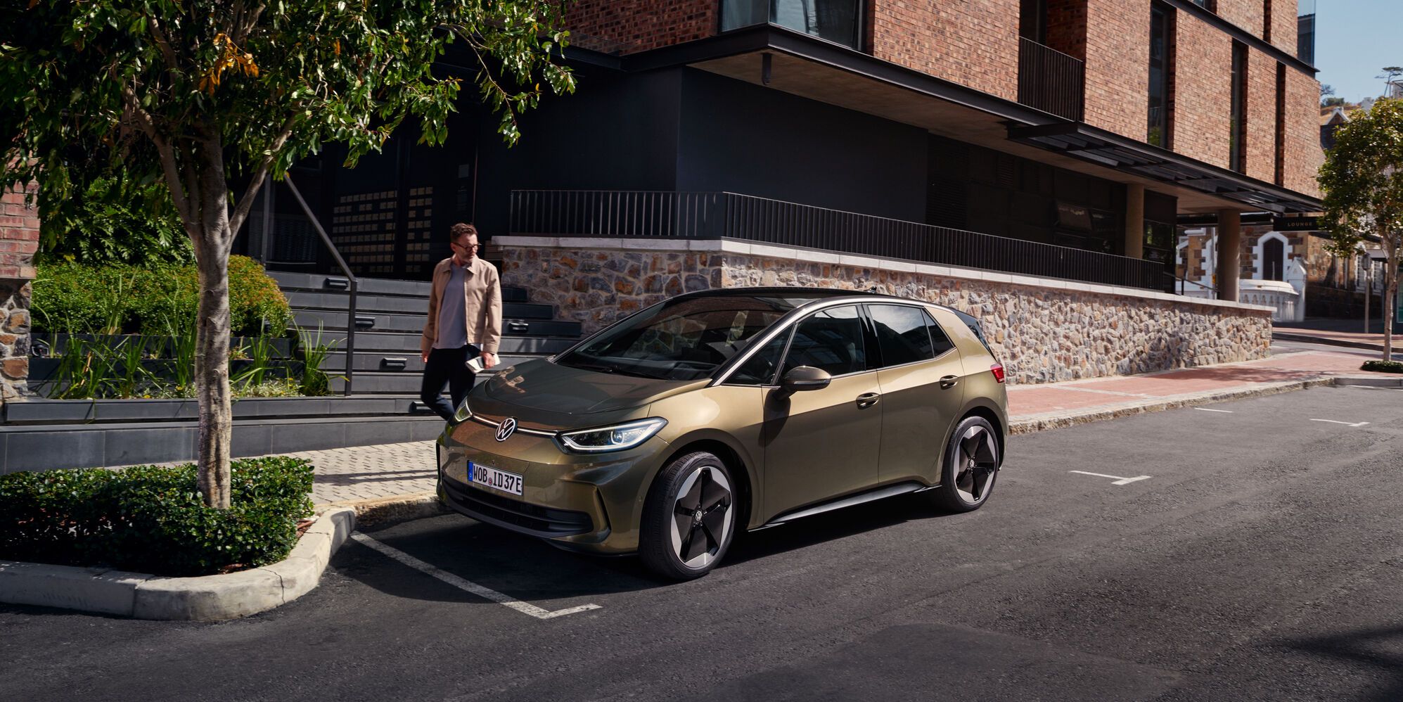 Поглед към VW ID.3 в цвят "Dark Olivine Green Metallic", паркиран отстрани на улица, до бордюра.