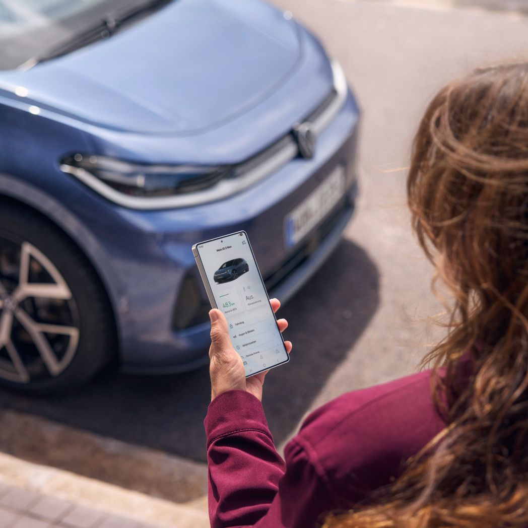 Жена гледа смартфона си, пред нея е паркиран син VW ID.3 Neo