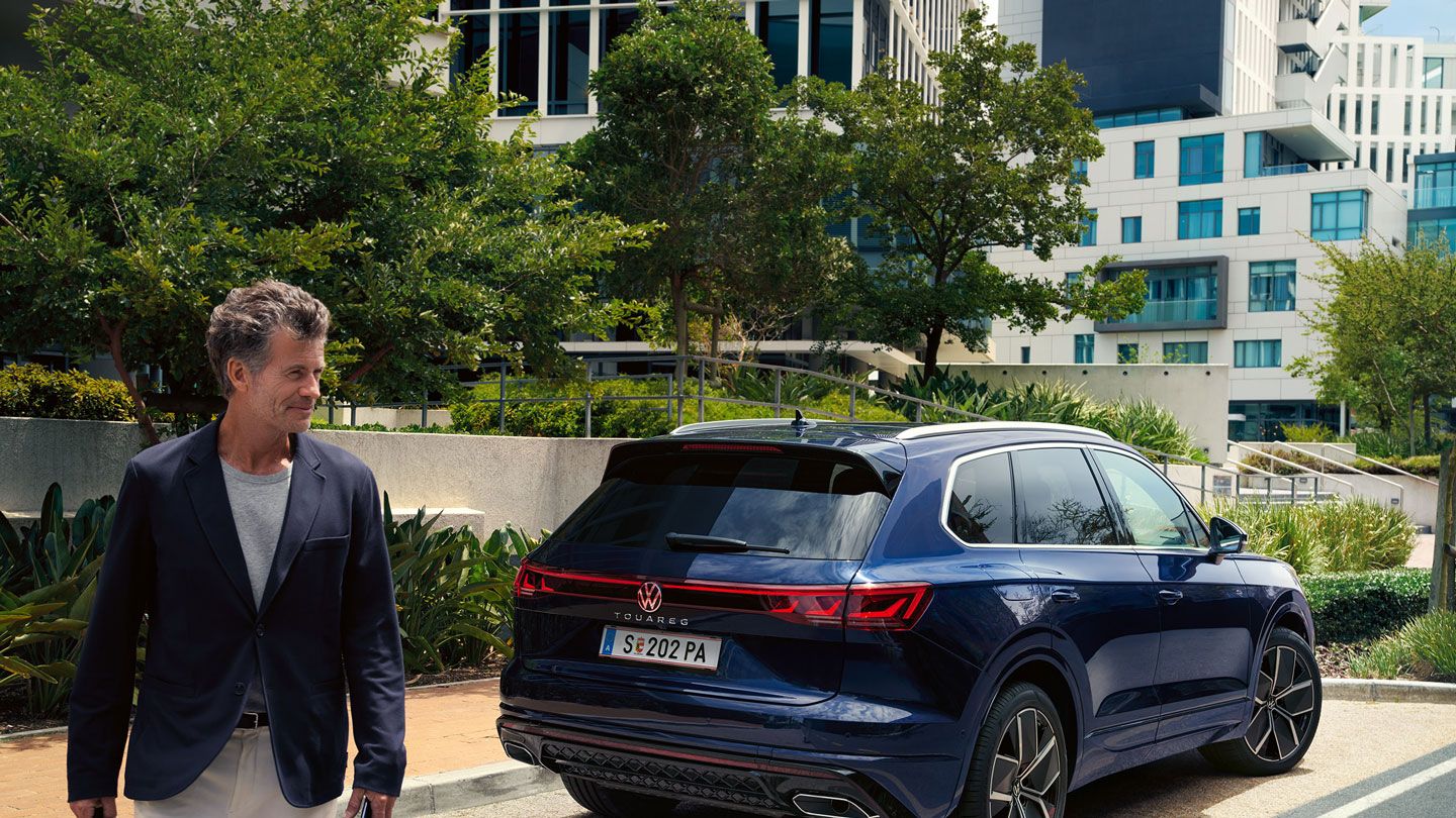 Мъж пресича улицата, косо зад него VW Touareg R-Line, паркиран отстрани на пътя.