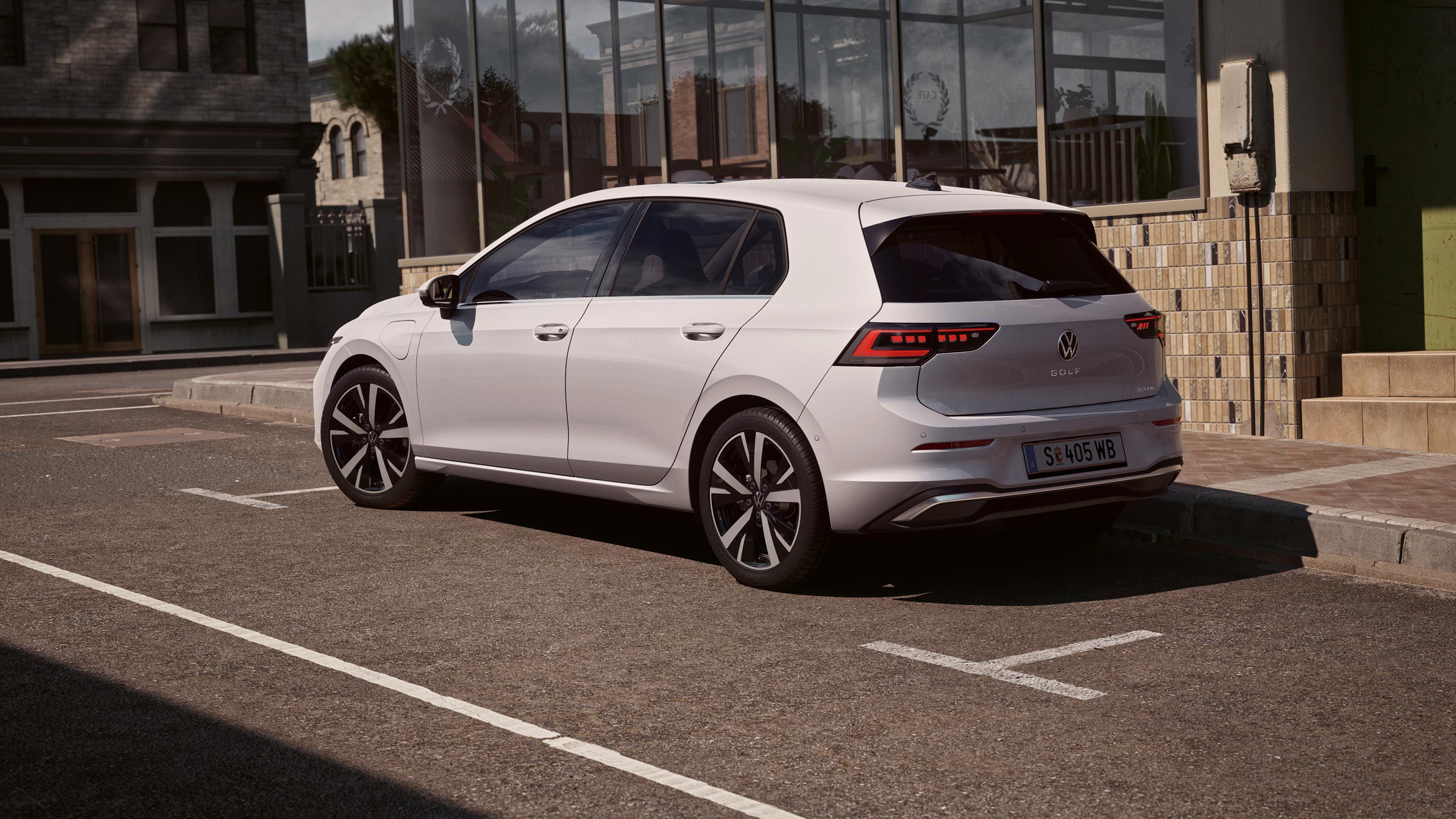Seitenansicht weißer VW Golf, welches neben einem Restaurant parkt. Ein Mann bewegt sich von der Tür des Restaurants in Richtung des Wagens.
