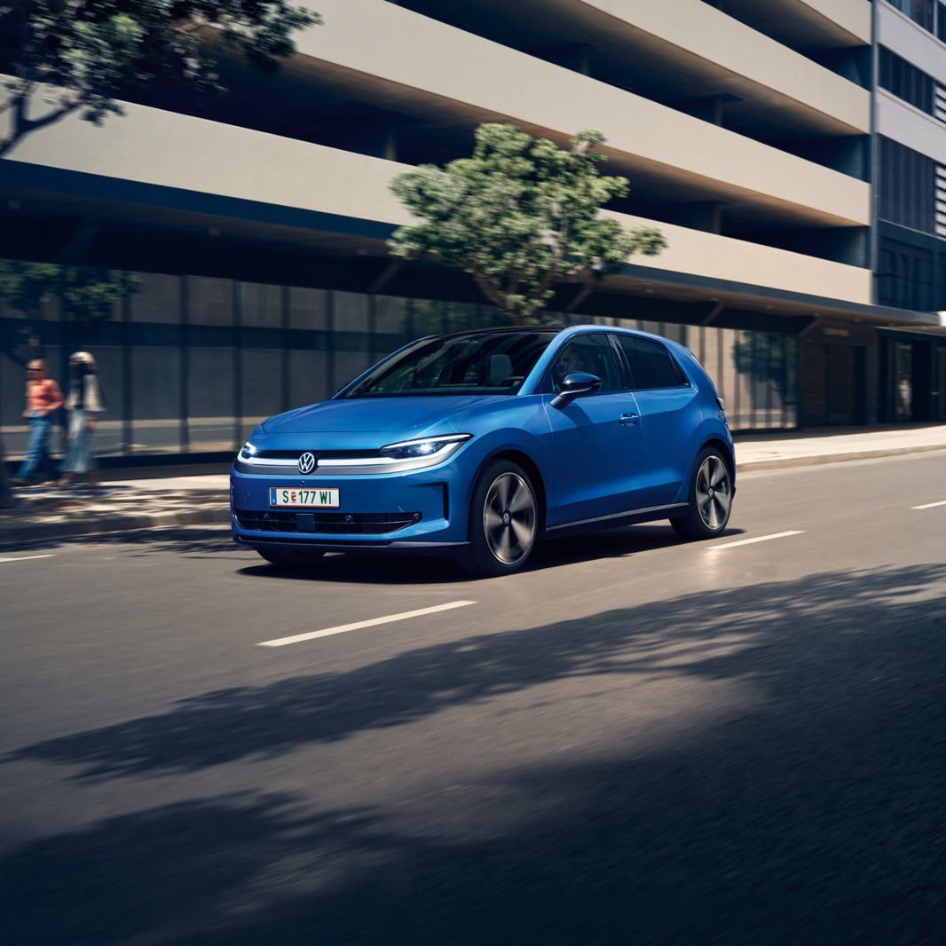 Син VW ID. Polo Style минава през град с зелени дървета край пътя.