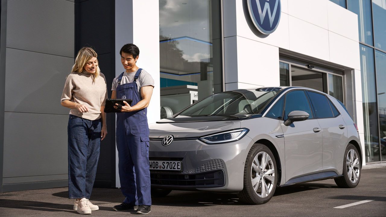 Мъж с таблет обяснява на жена, застанали пред спрял пред VW комплекс ID.3 автомобил