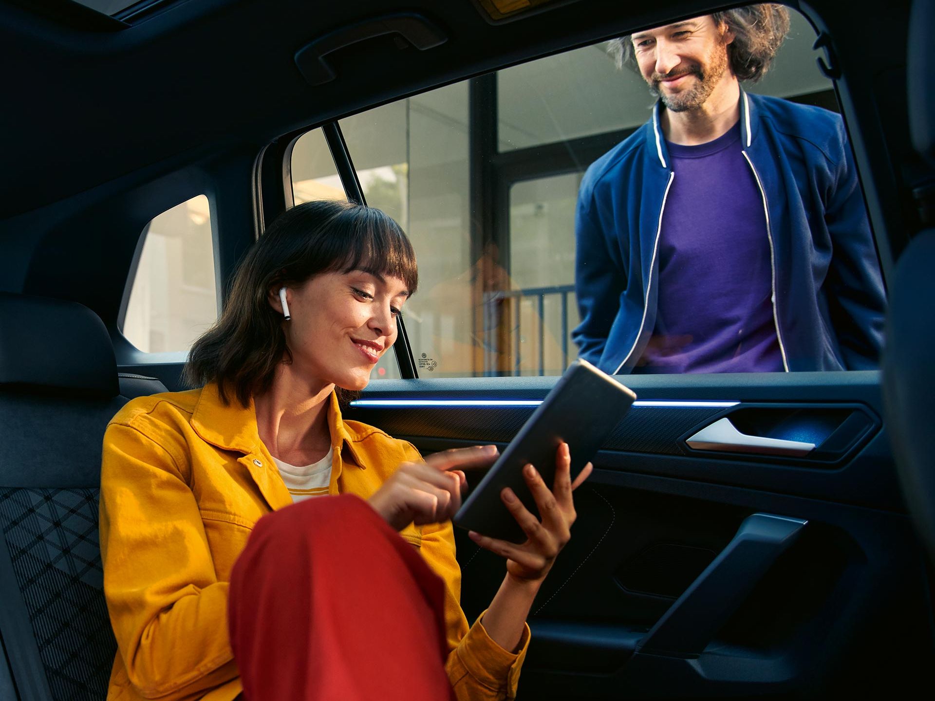 Жена седи на задната седалка на VW Tiguan и използва We Connect чрез таблет